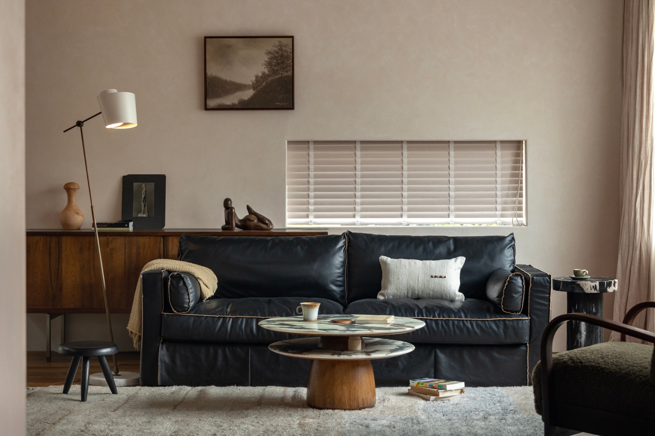 A cup rests on a tiered marble coffee table positioned in front of a dark leather sofa in a modern living room.