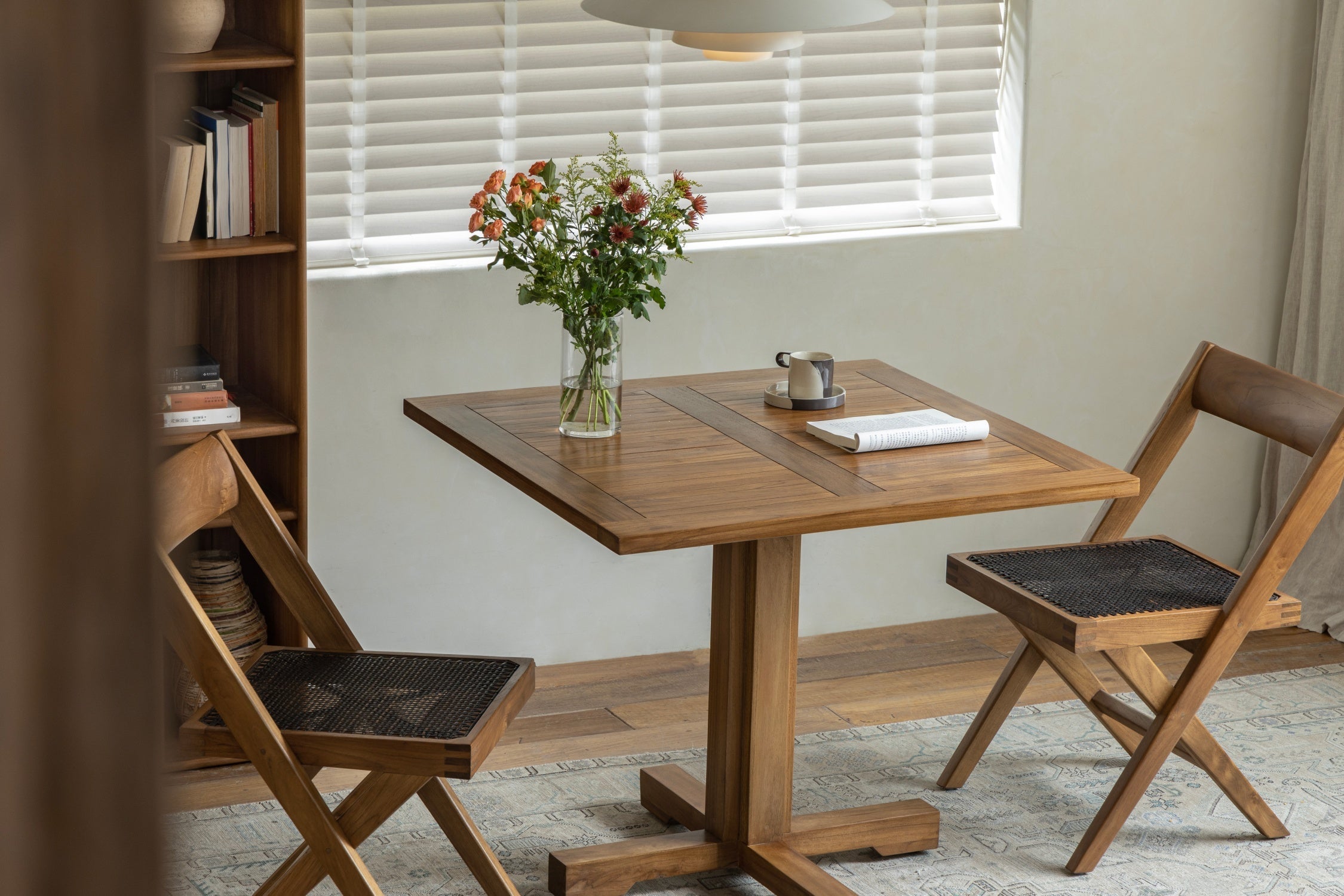 A simple yet inviting dining area featuring a wooden table with a vase of flowers, accompanied by two wooden chairs, creating a warm and comfortable atmosphere.