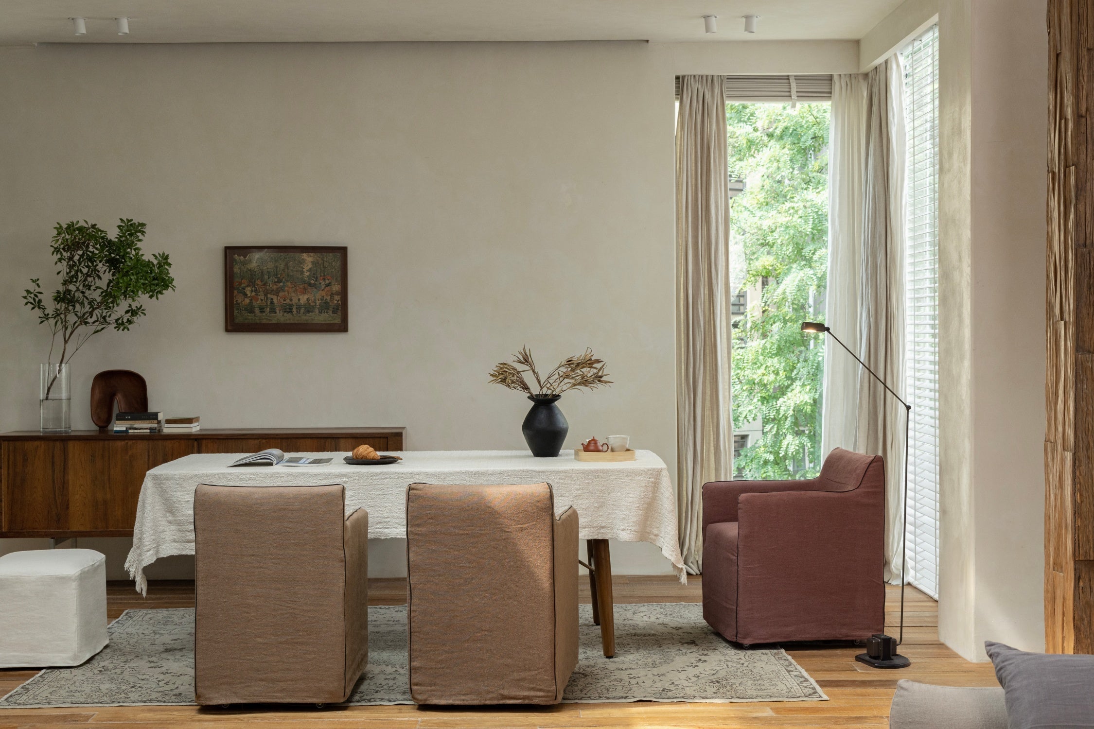 Bright dining room with upholstered chairs, a wood table, pink armchair, and floor-to-ceiling windows
