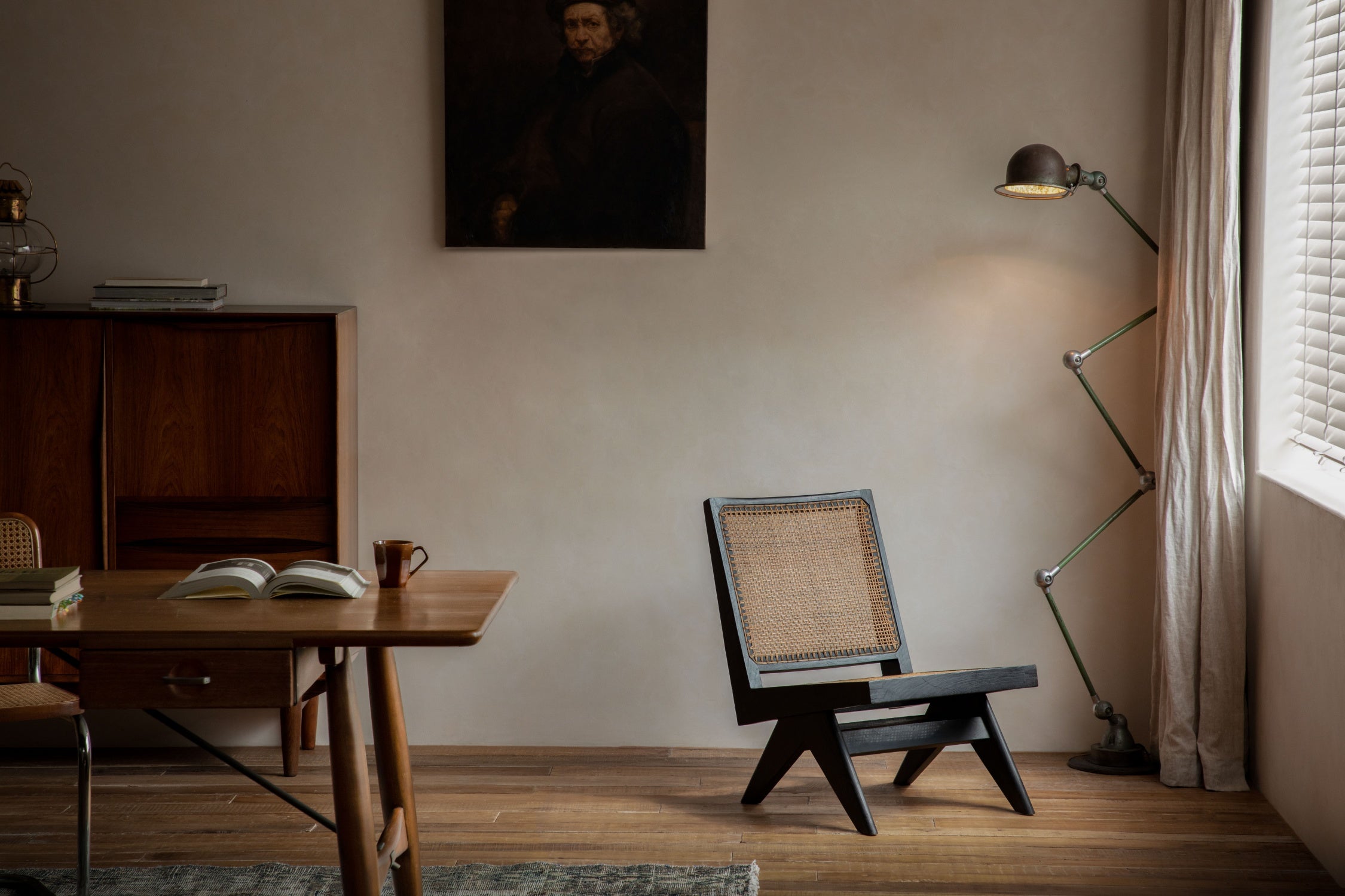 A low-profile armless chair with a woven rattan back stands in a quiet room beside an adjustable floor lamp.