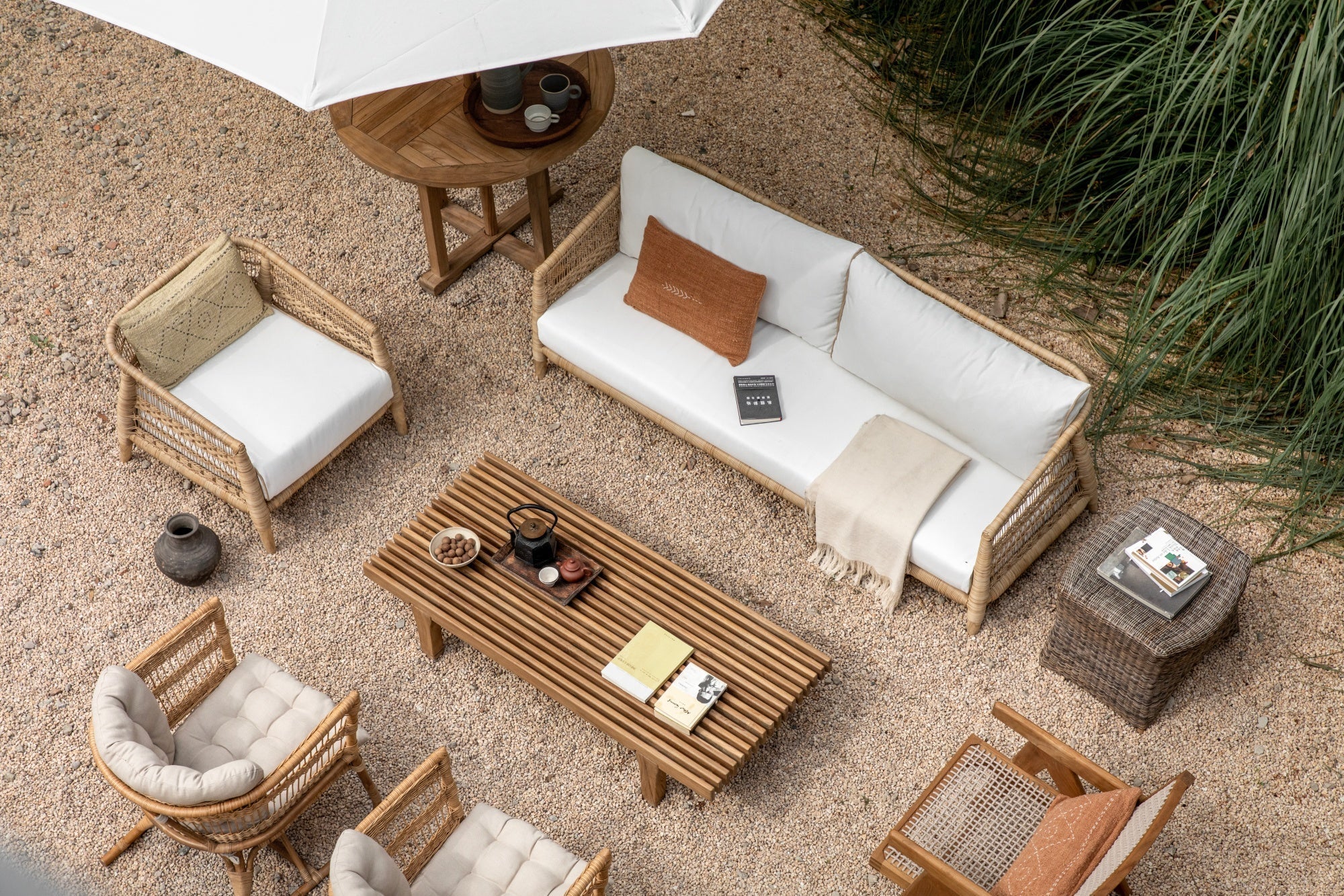 Overhead view of a wooden outdoor furniture set on gravel with a sofa, armchairs, coffee table, and lush greenery