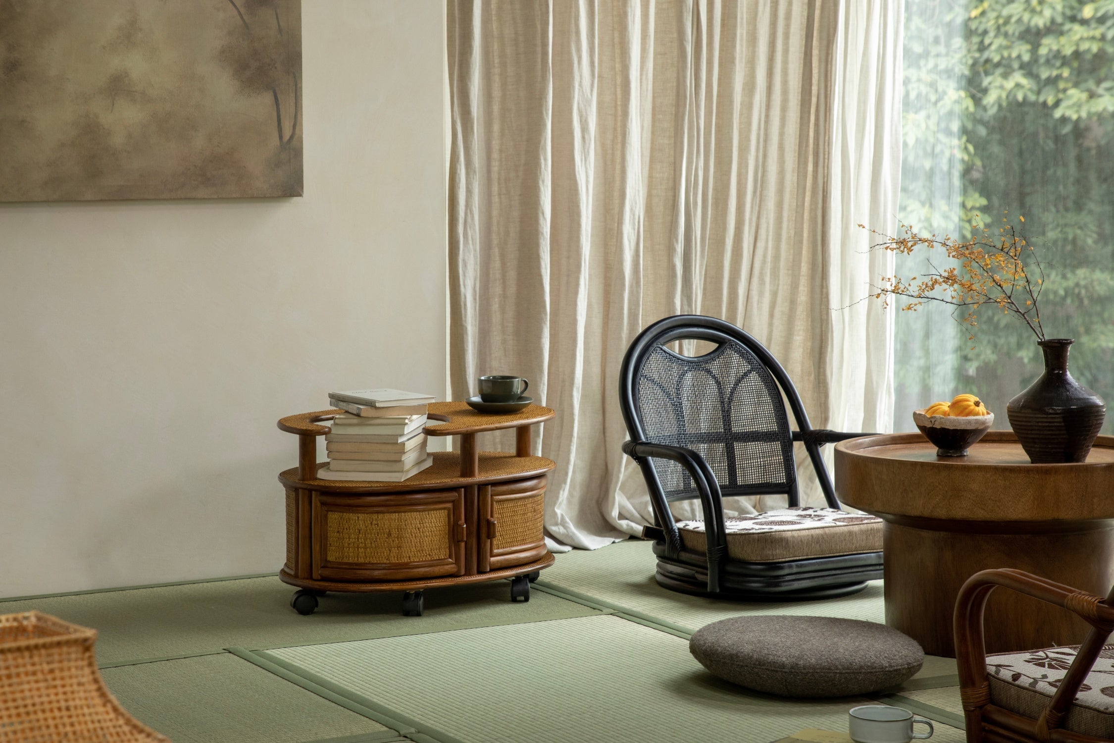 A rolling rattan side table with a stack of books sits in a serene room near a black accent chair and a wooden coffee table.