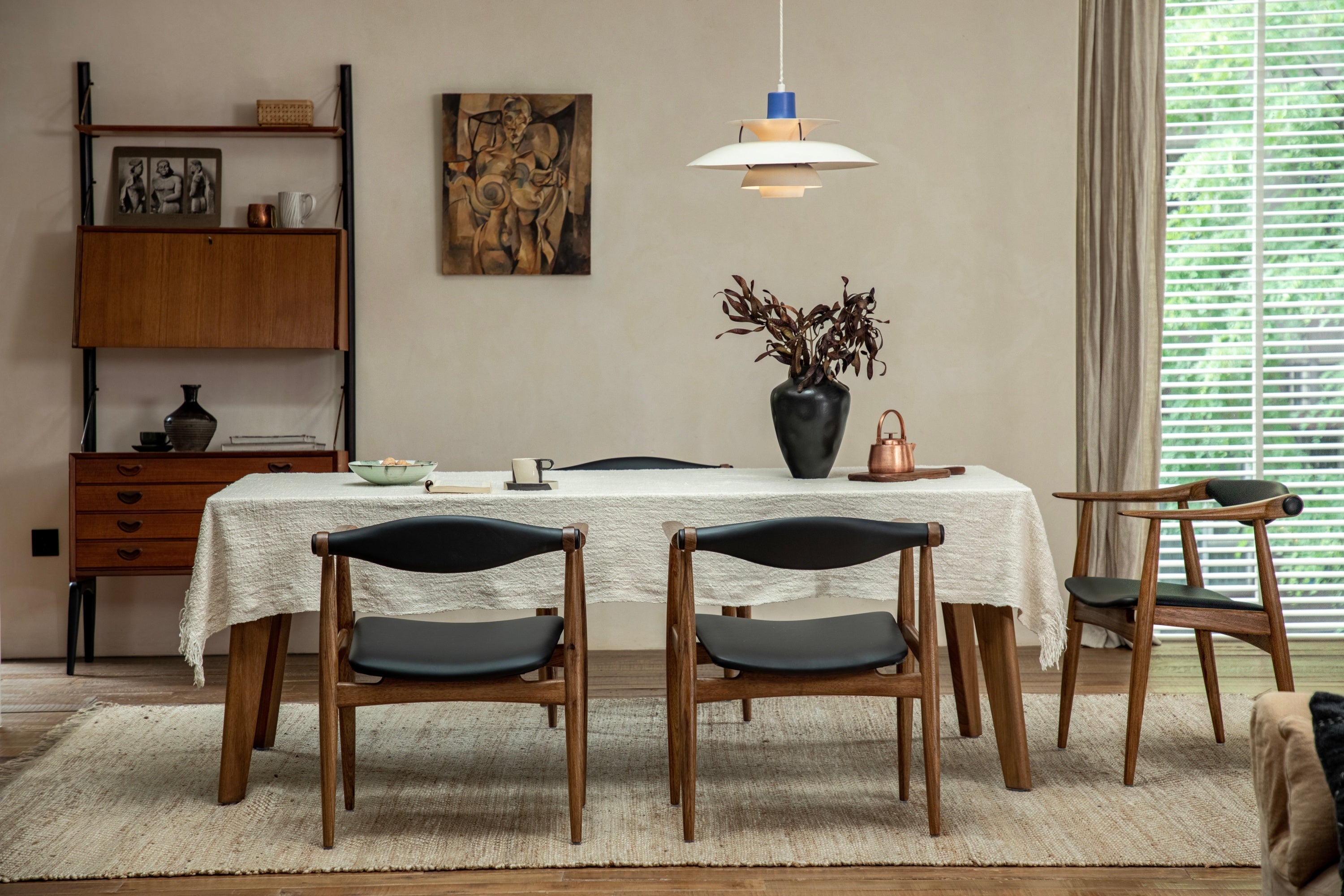 Dining table with four chairs, a white tablecloth, and a vase with dried flowers in a cozy room.