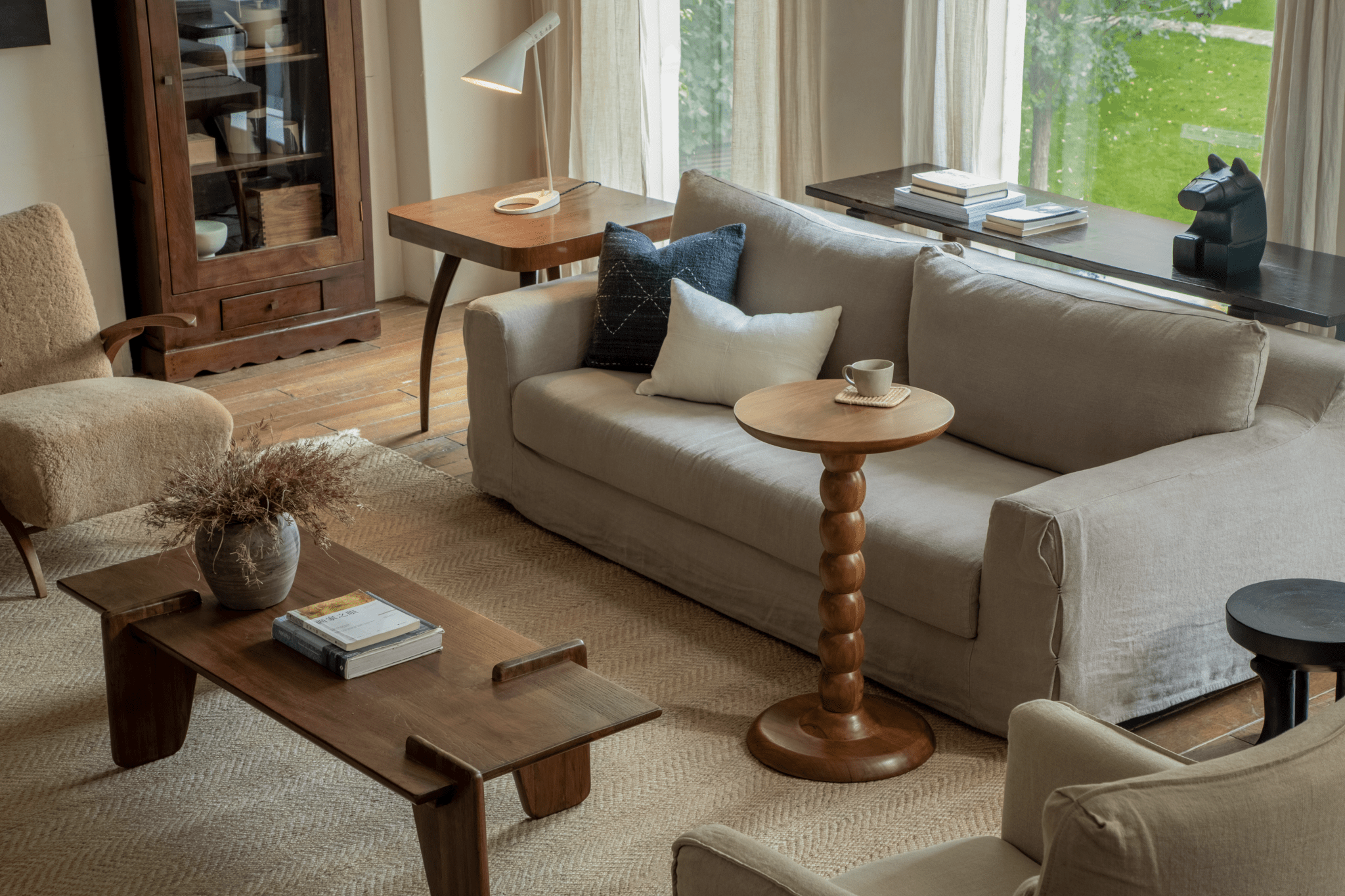 Neutral living room with cream sofa, wooden coffee table, and round side tables by large windows