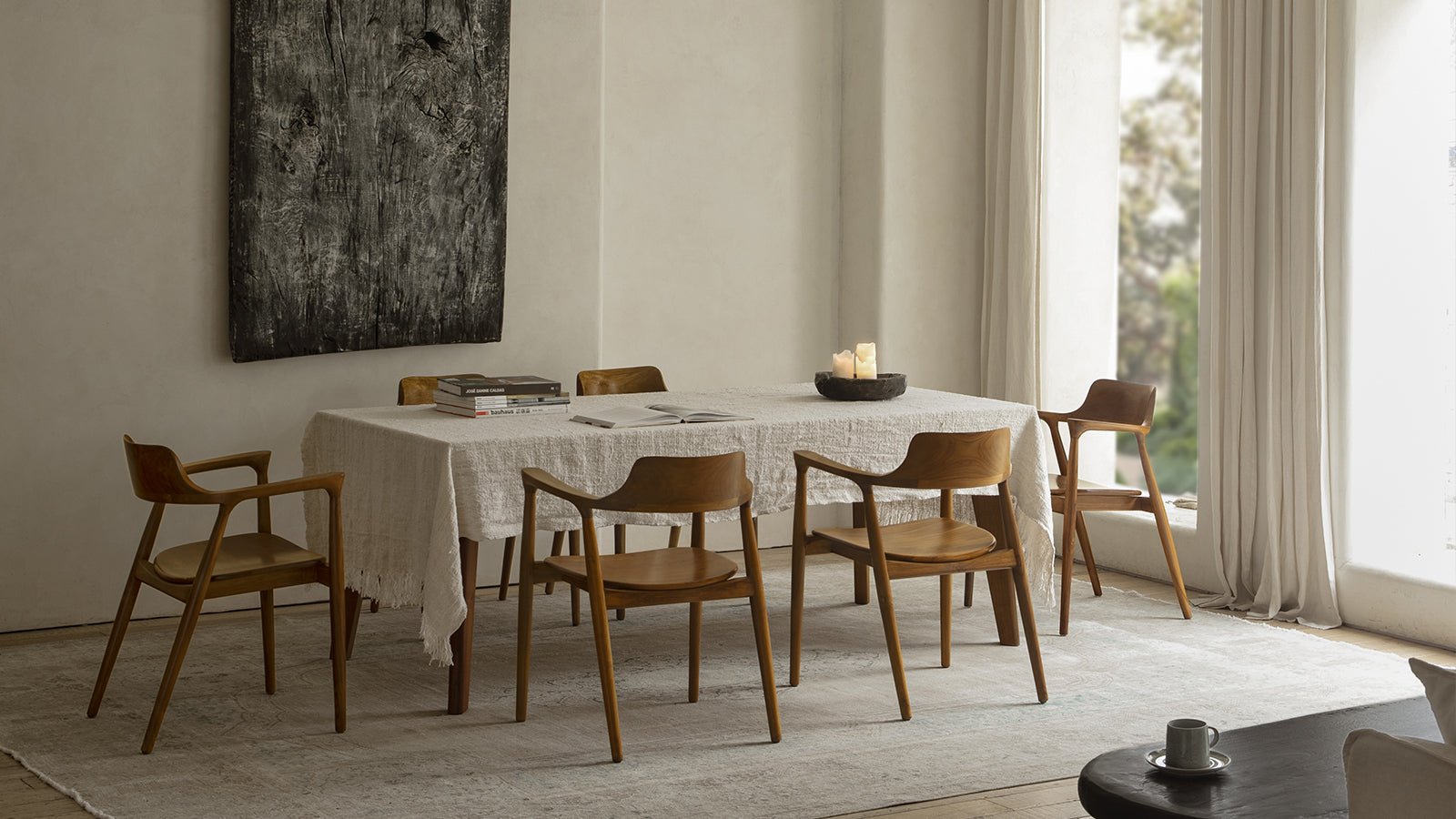 A bright, airy dining room with mid-century modern wooden chairs surrounding a table with a white linen tablecloth