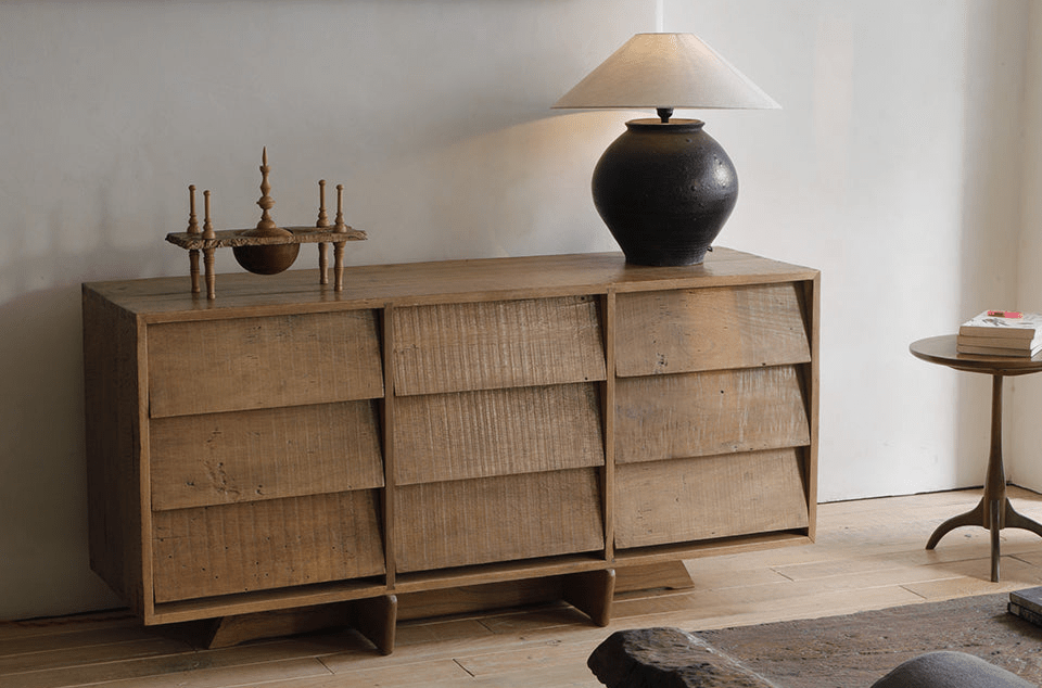 Elegant wooden sideboard with textured front panels crafted from reclaimed wood, displaying a black ceramic lamp and brass accents in a minimalist interior.