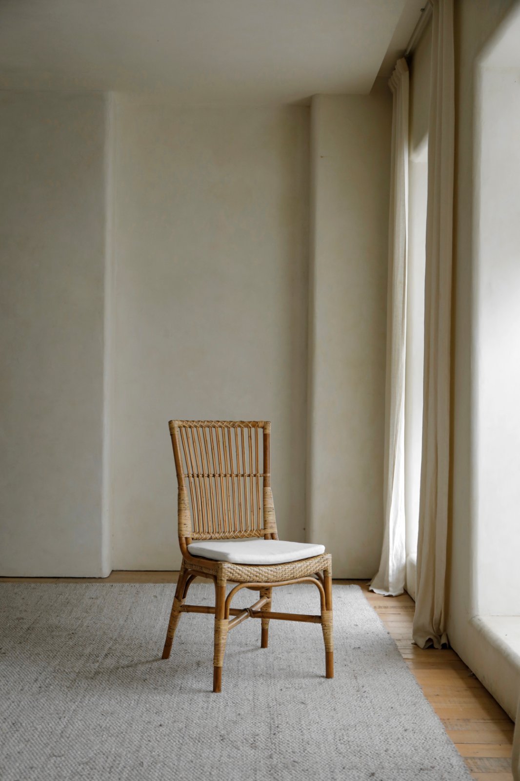 Axis Chair made of Indonesian rattan with a white cushion on a grey rug in a well-lit room.
