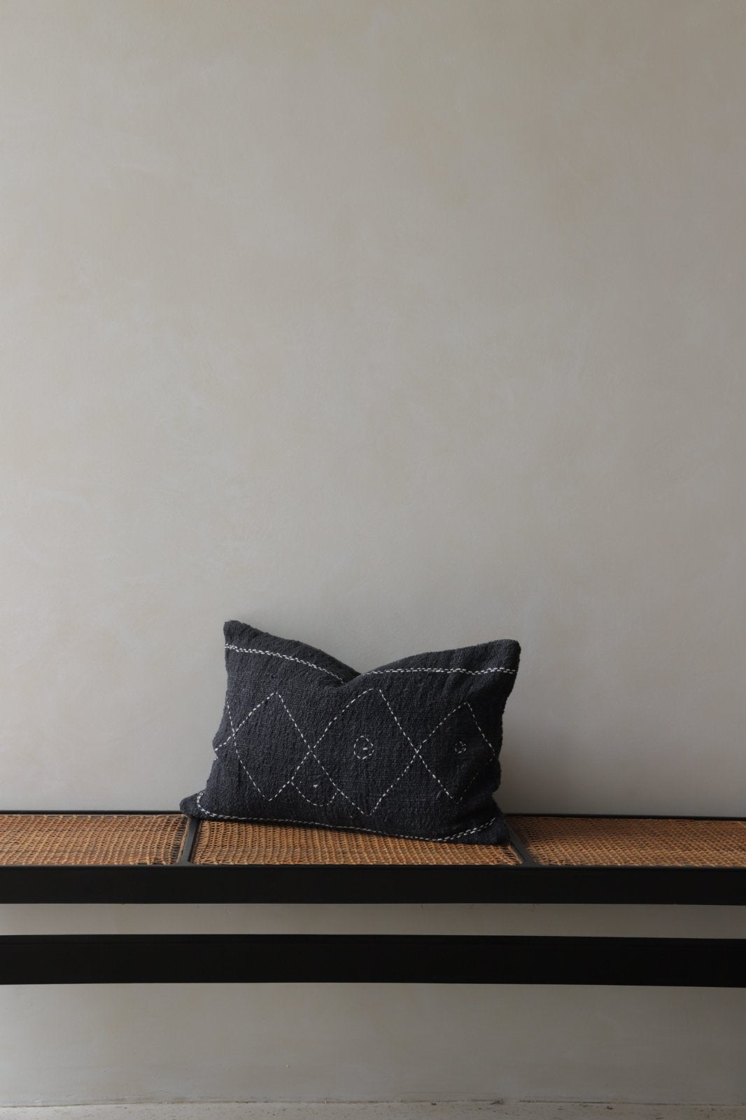 Cotton pillow with geometric stitching, dark gray color, on a woven bench, part of a modern home decor.
