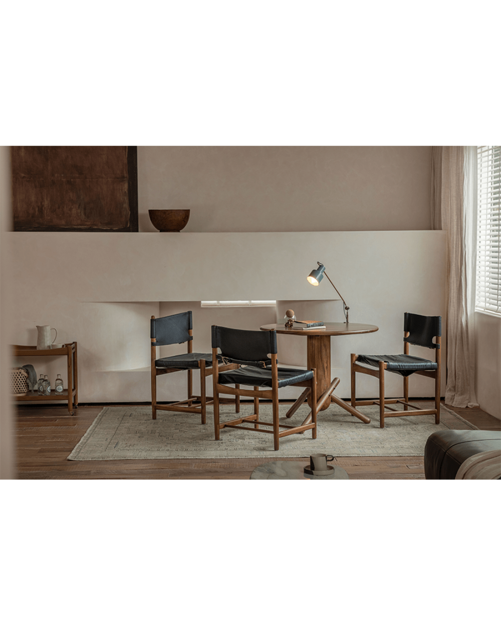 Spanish Dining Chairs with black leather seats and teak wood frames around a wooden dining table in a neutral room.