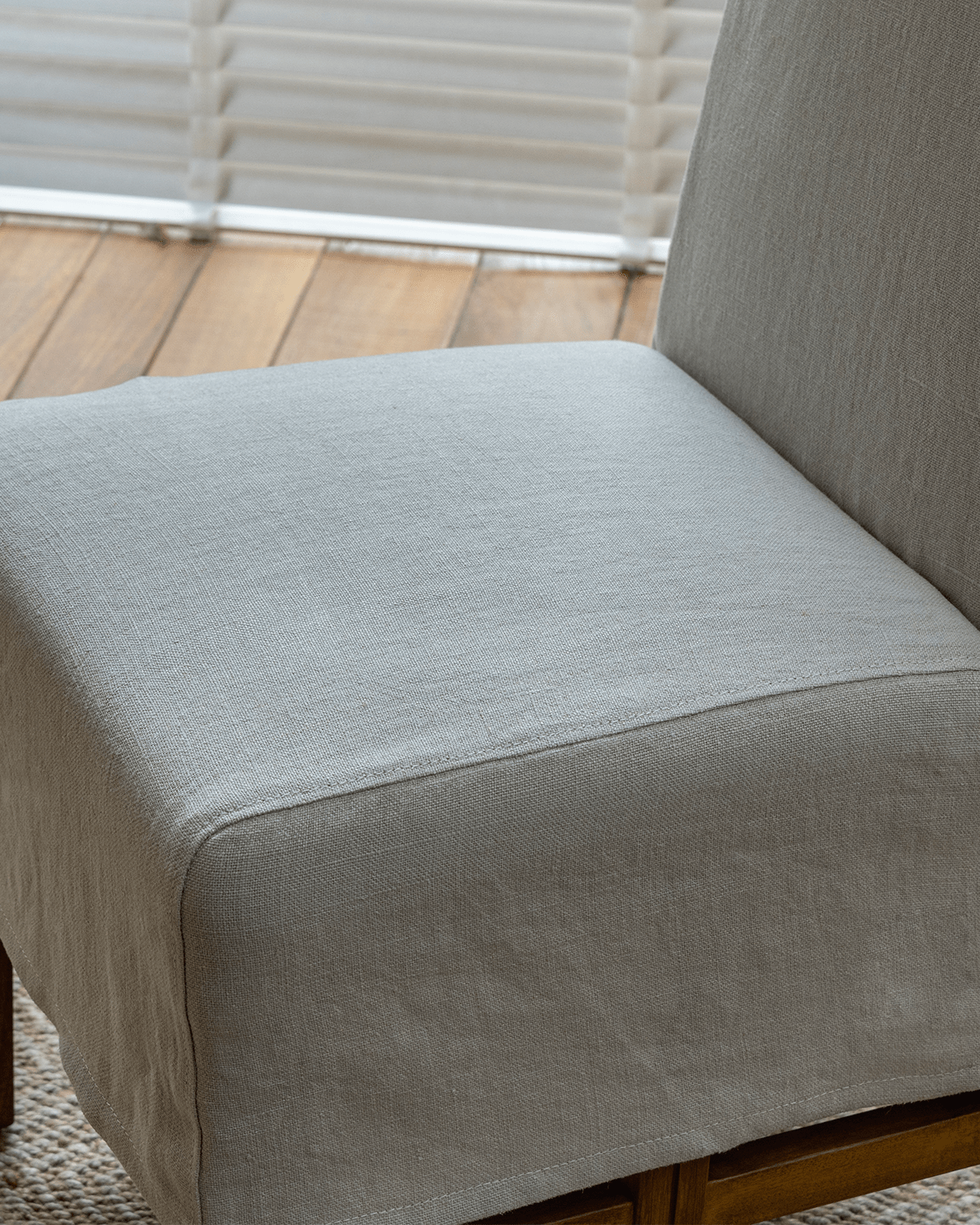 Feast Dining Chair detail: Light gray linen slipcover with wood frame, showcasing neutral tones and modern design.