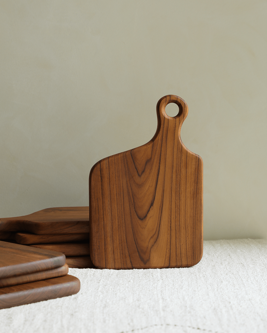 Durable teak wood cutting board with hanging hole and natural wood grain pattern.