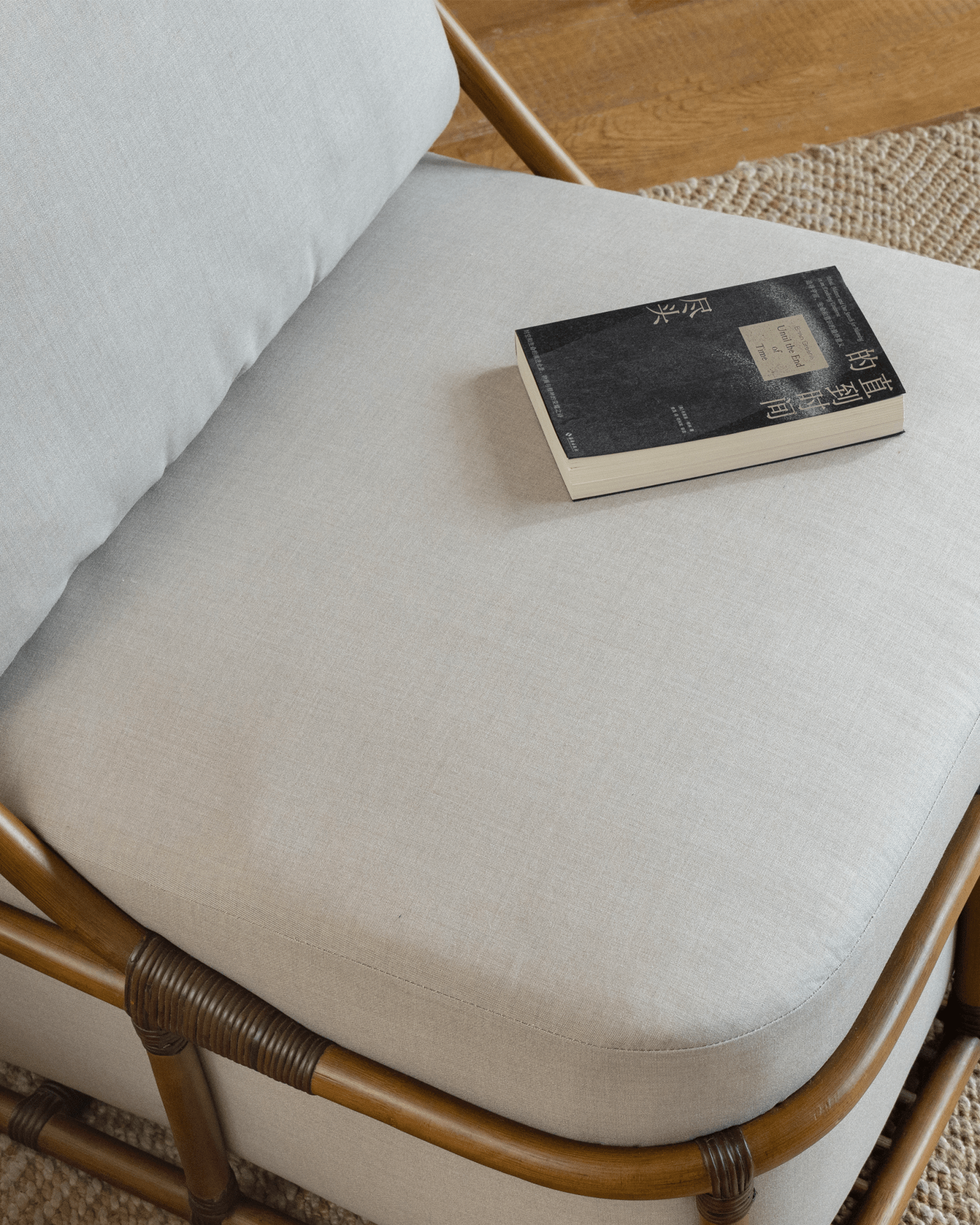 Tofu Lounge Sofa detail with book. Natural rattan frame, light gray cushion, and book. Promoting relaxed seating.
