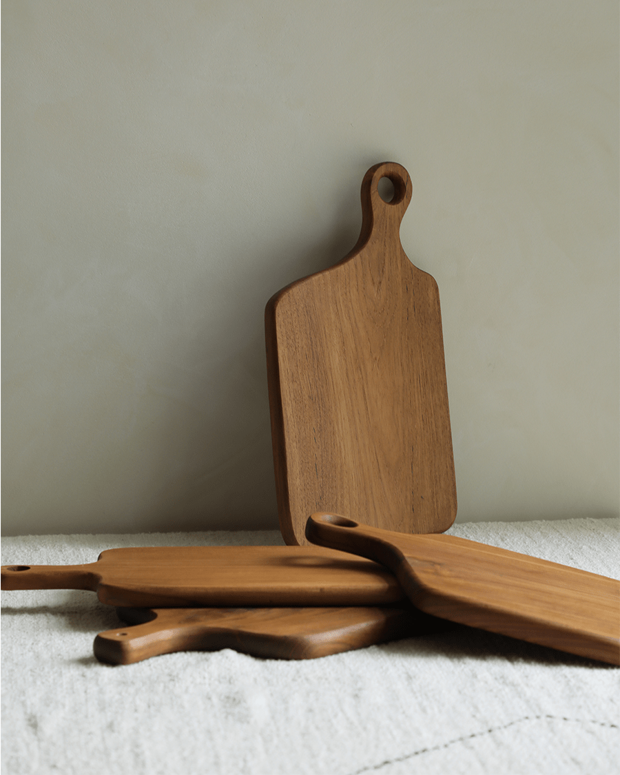 Handcrafted teak cutting board with hanging hole, natural wood grain.