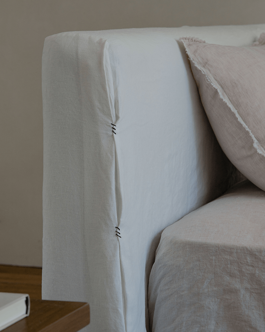 Freya Linen Bed headboard detail: White linen upholstery, stitching, and a soft pink pillow for peaceful sleep.
