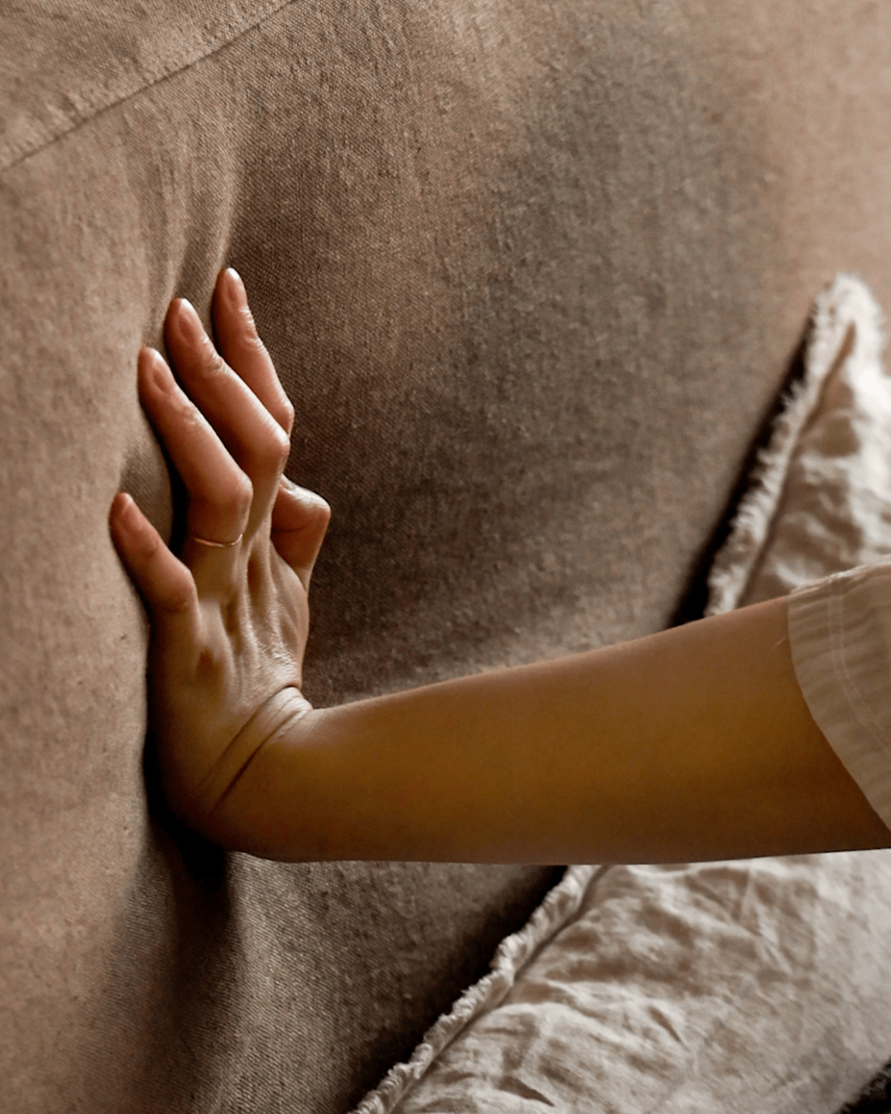 Hand on Freya Linen Bed, showcasing natural linen upholstery's texture and soft cushioning for peaceful sleep.