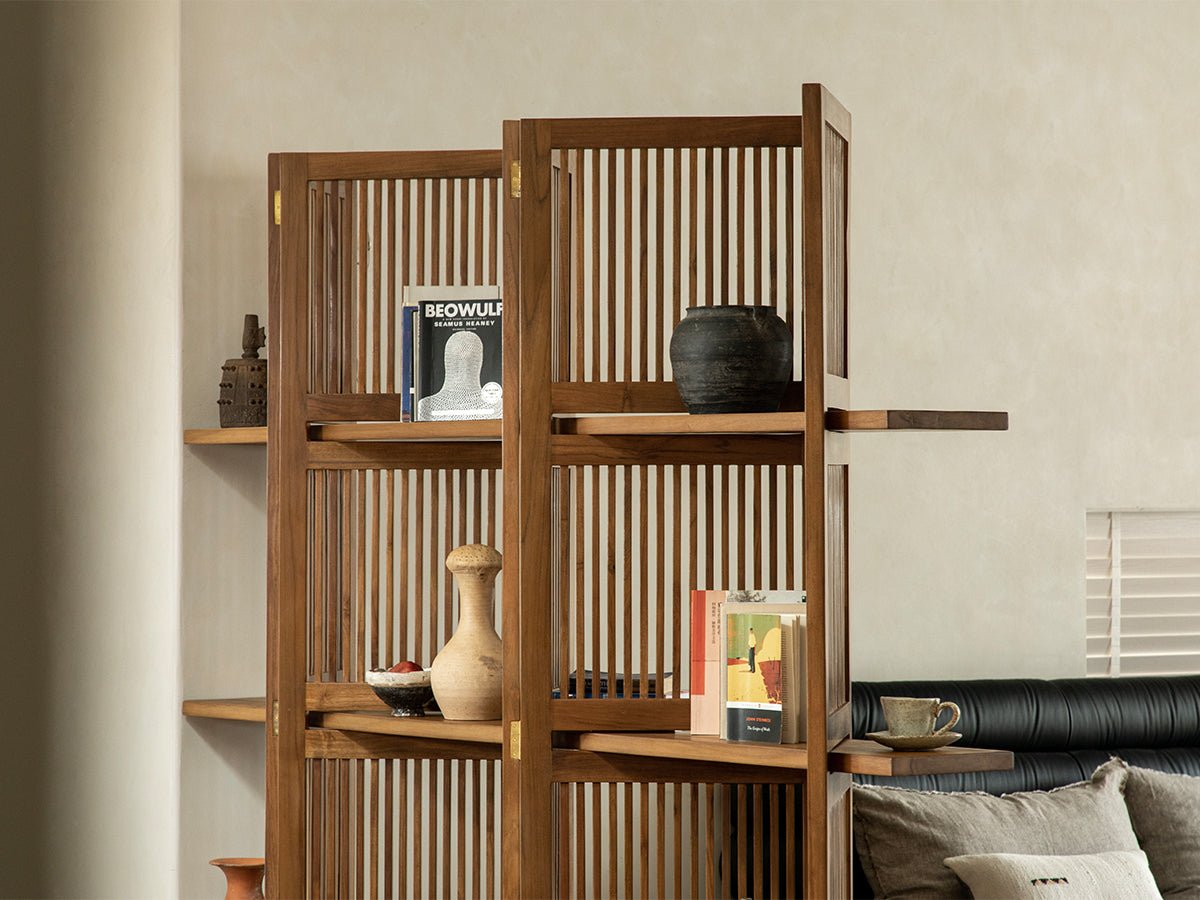 Sylvan teak room divider with slatted panels and integrated shelves, styled with books and decor.