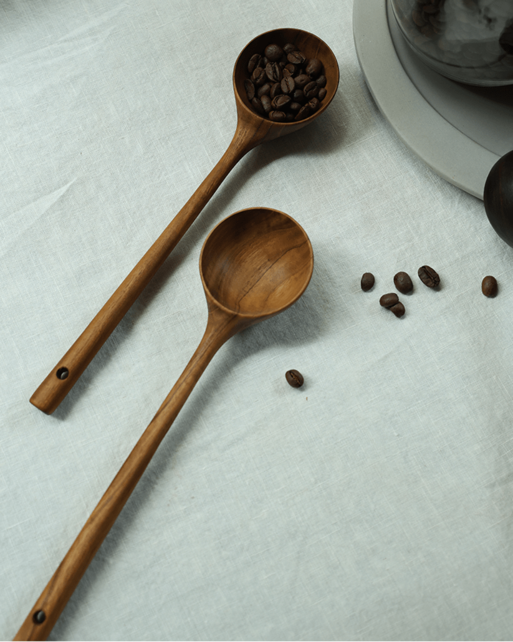 Teak coffee spoons on linen surface, one filled with coffee beans, ideal for serving coffee.