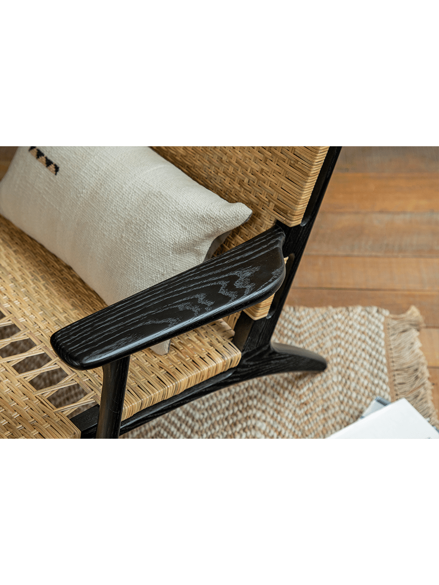 Horn Lounge Chair detail: black oak armrest, natural rattan seat, and pillow, ergonomic design, handcrafted for comfort.