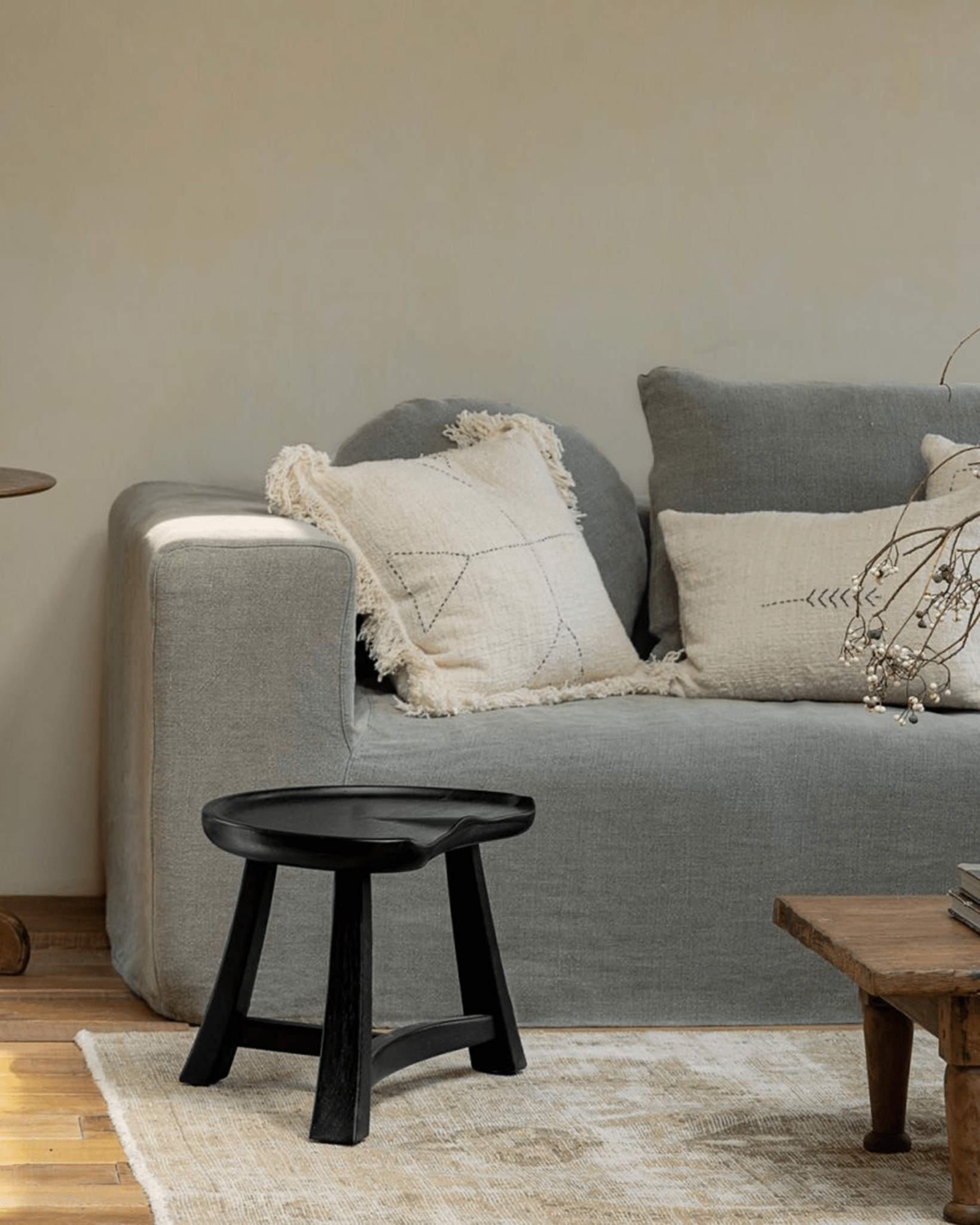 Black Pod Stool in living room setting. Teak stool serves as side table in a vintage or modern interior with sofa and rug.