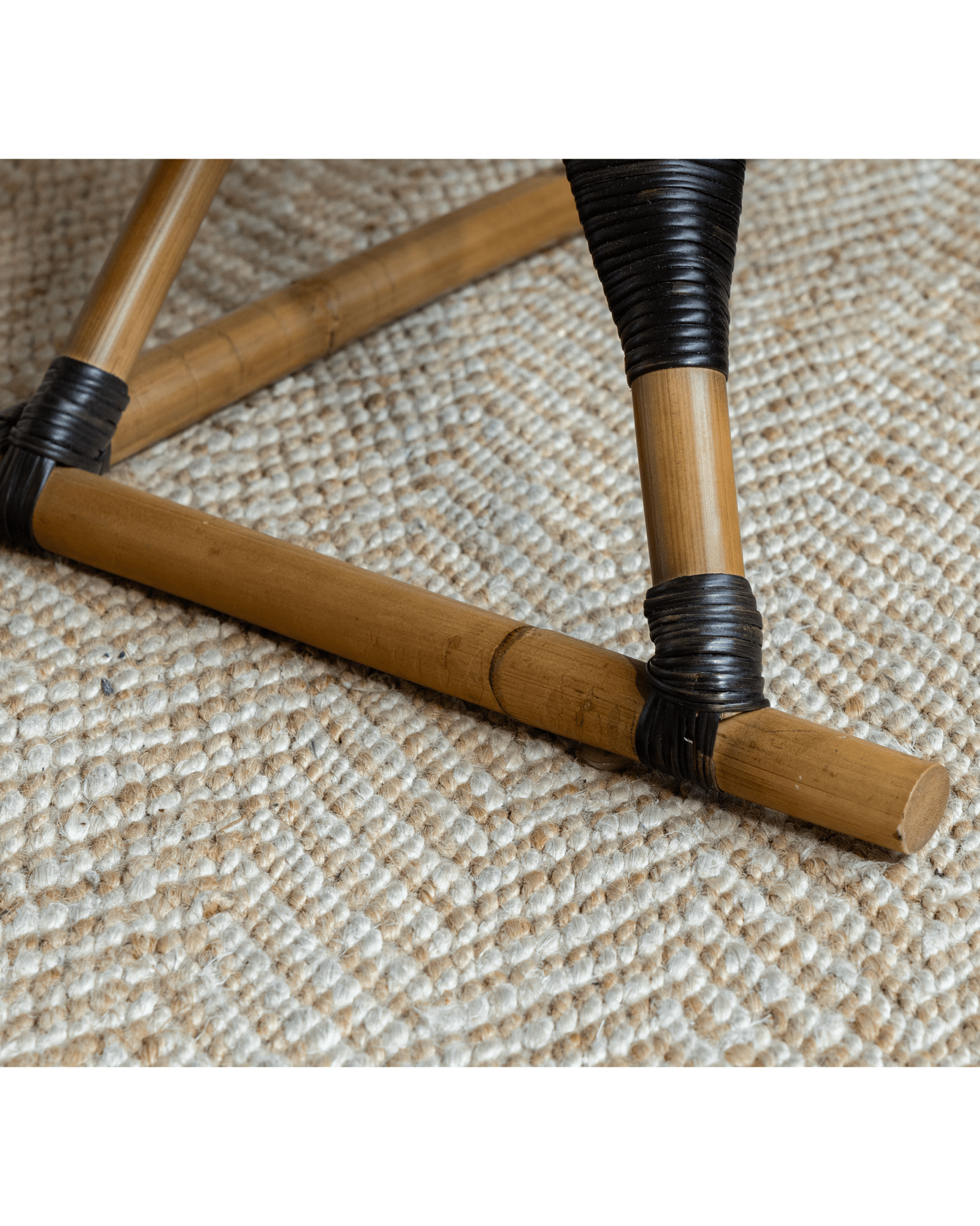 Helian Rattan Chair detail: natural rattan legs with black accents, handcrafted design and gray cushion, cozy interior.