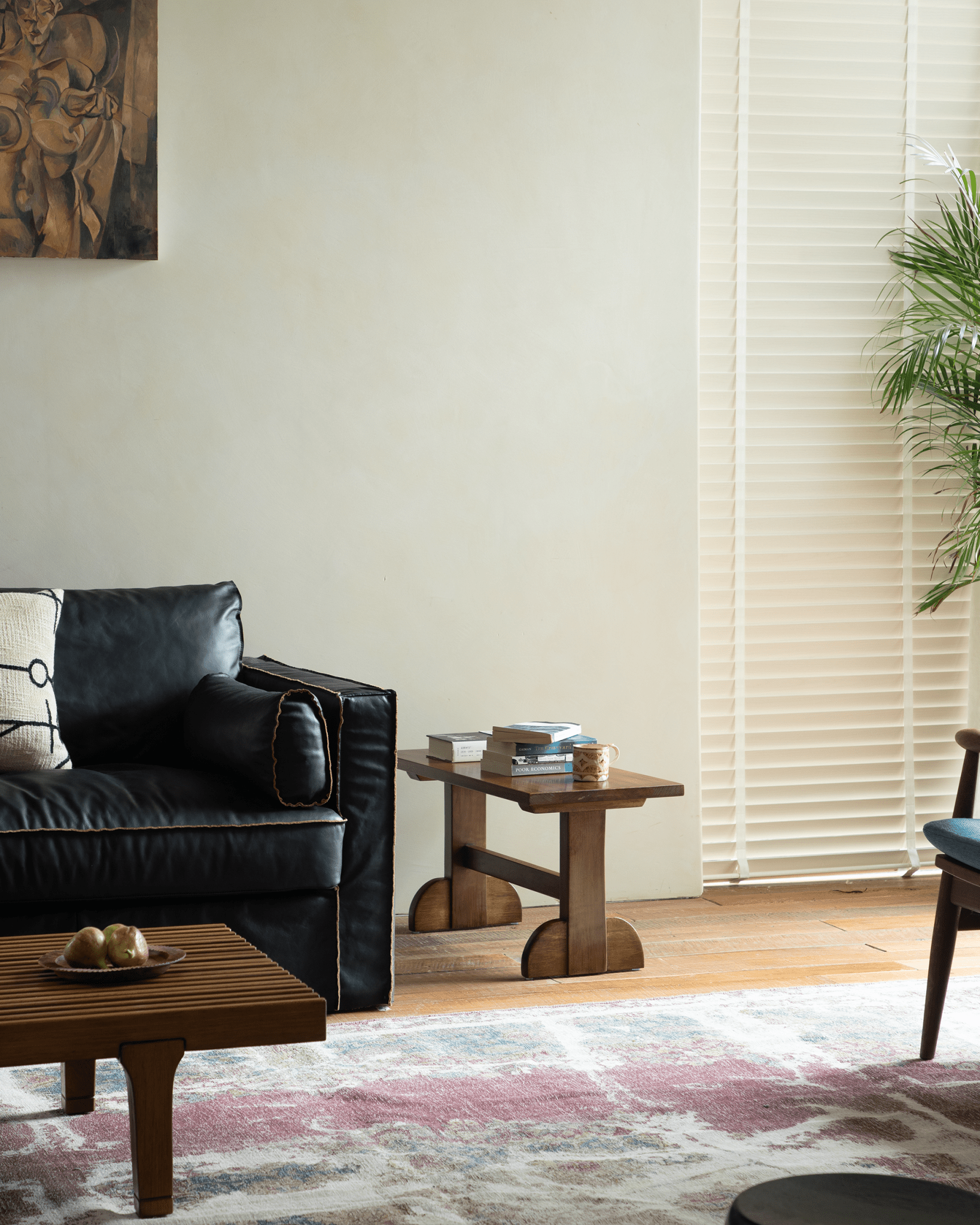 Hoof Side Table in a living room setting, nanmu wood, with books and coffee cup, and a black leather sofa. Interior Design.