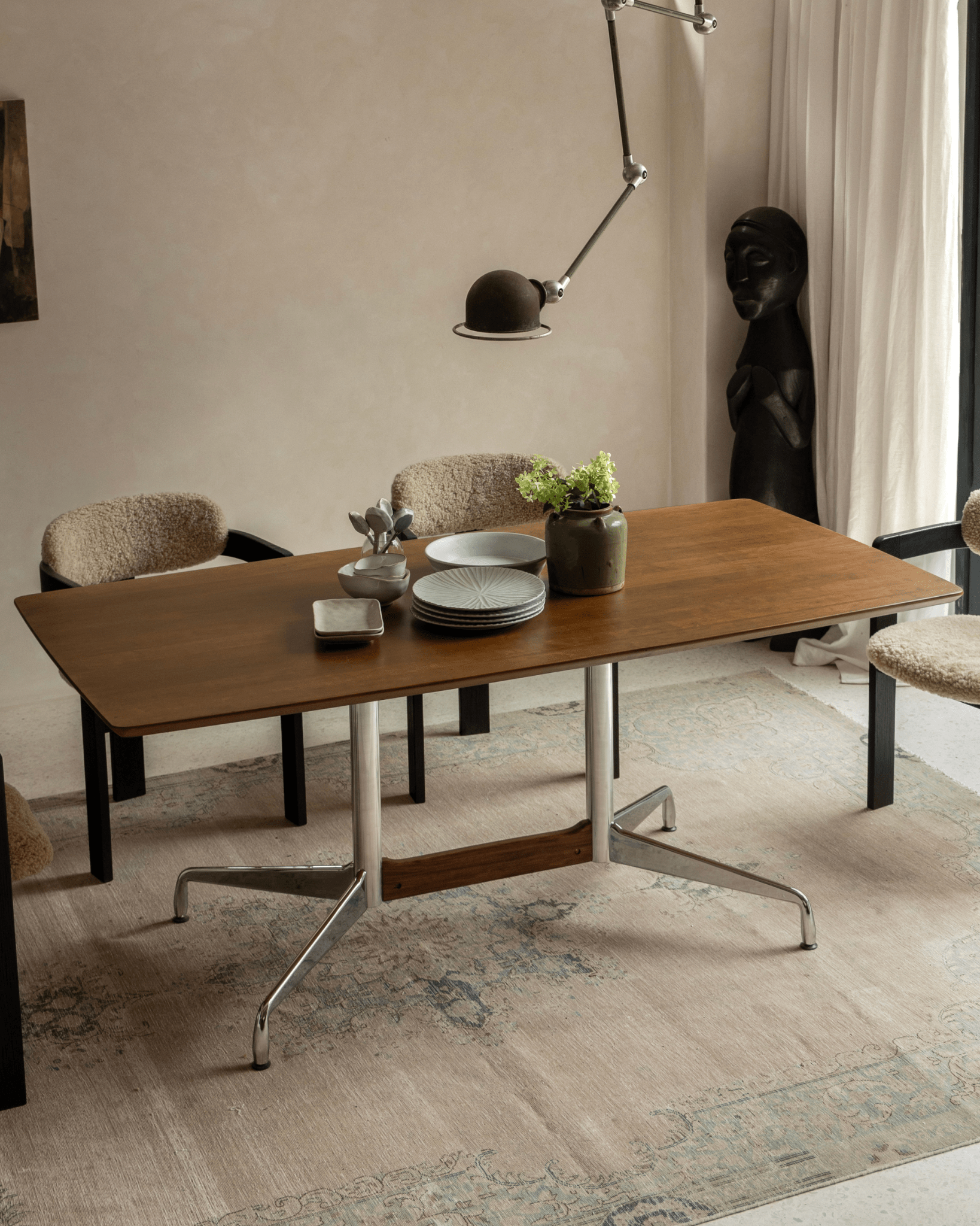 Eames desk with teak veneer top, aluminum legs, and mid-century modern design. Styled with tableware and greenery.