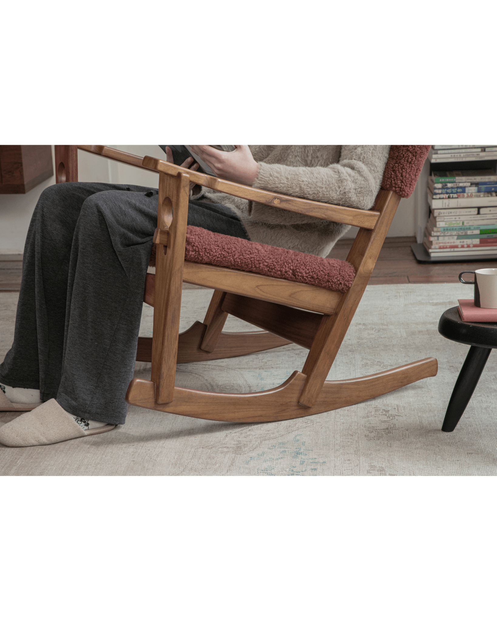 Hans rocking chair in Wine Red shearling and teak frame, person reading.