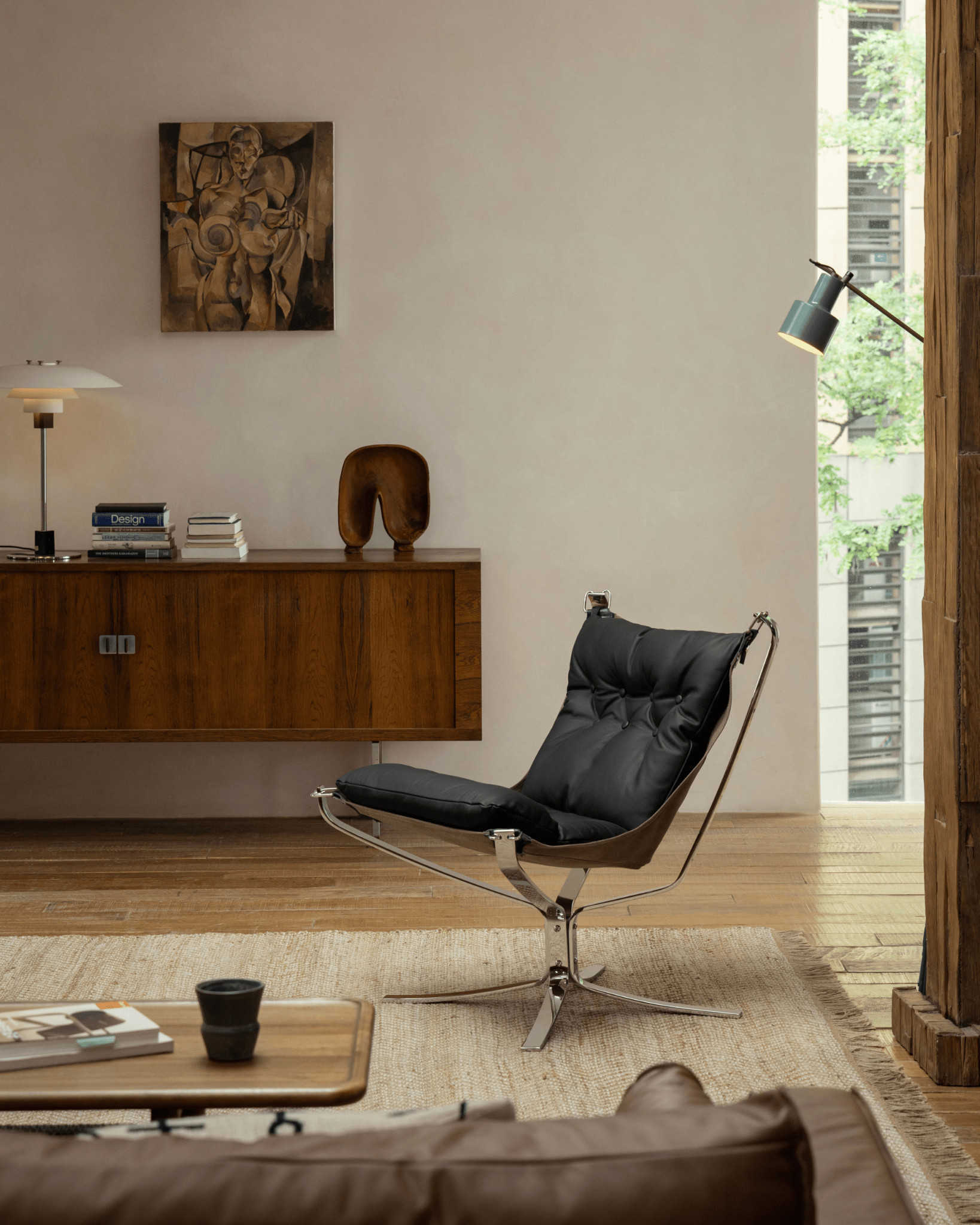 Black leather Falcon Chair with stainless steel frame in a modern living room setting, Scandinavian design, premium comfort.