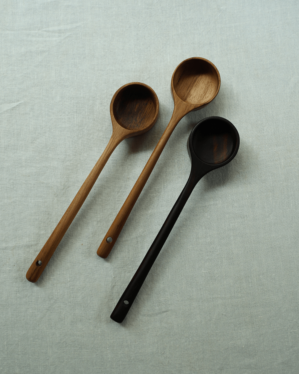 Teak coffee spoons in different wood tones displayed on a linen surface, perfect for coffee and serving.