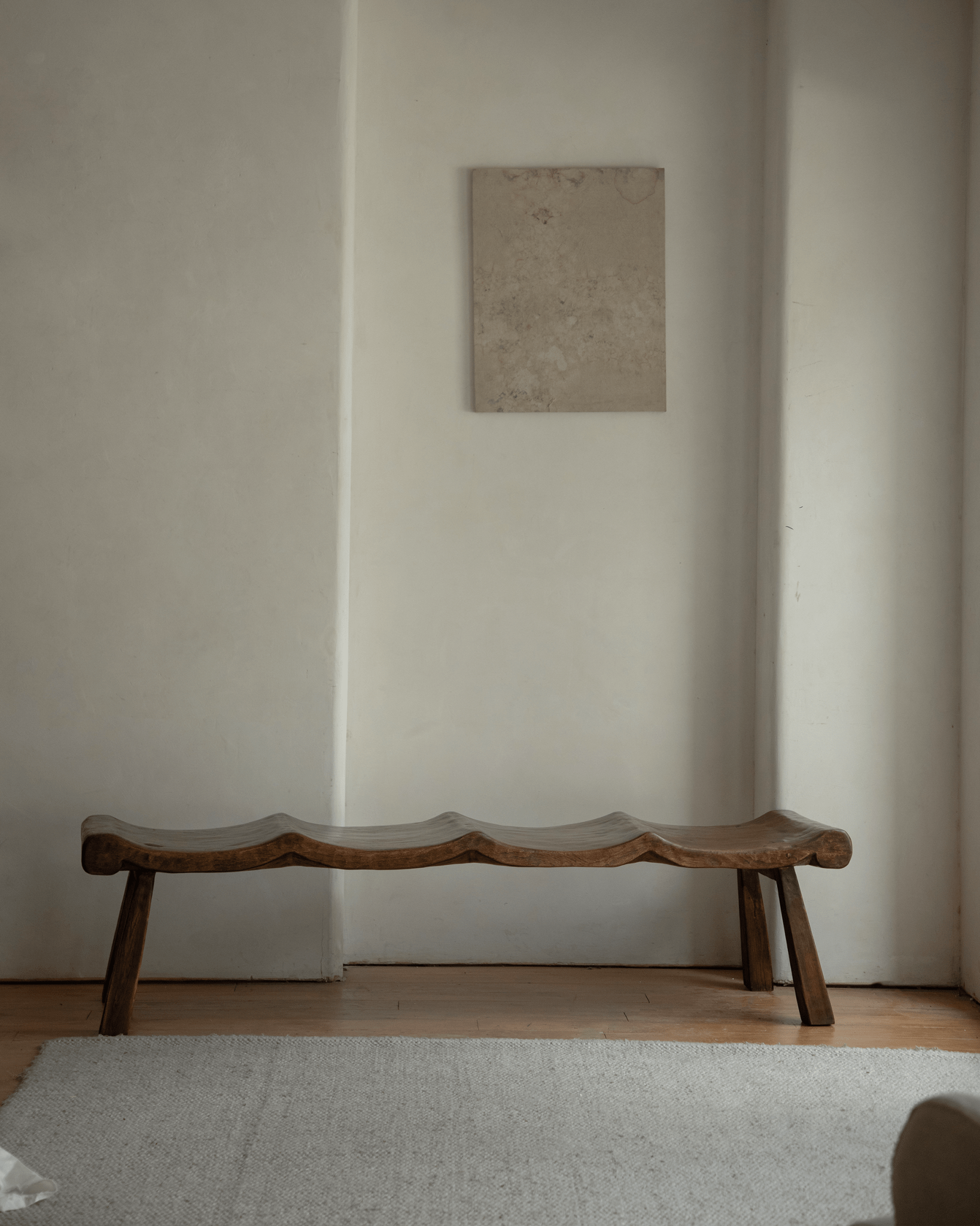 Tildes bench made of solid wood with a wave-like seat, brown color, set in a minimalist interior setting.