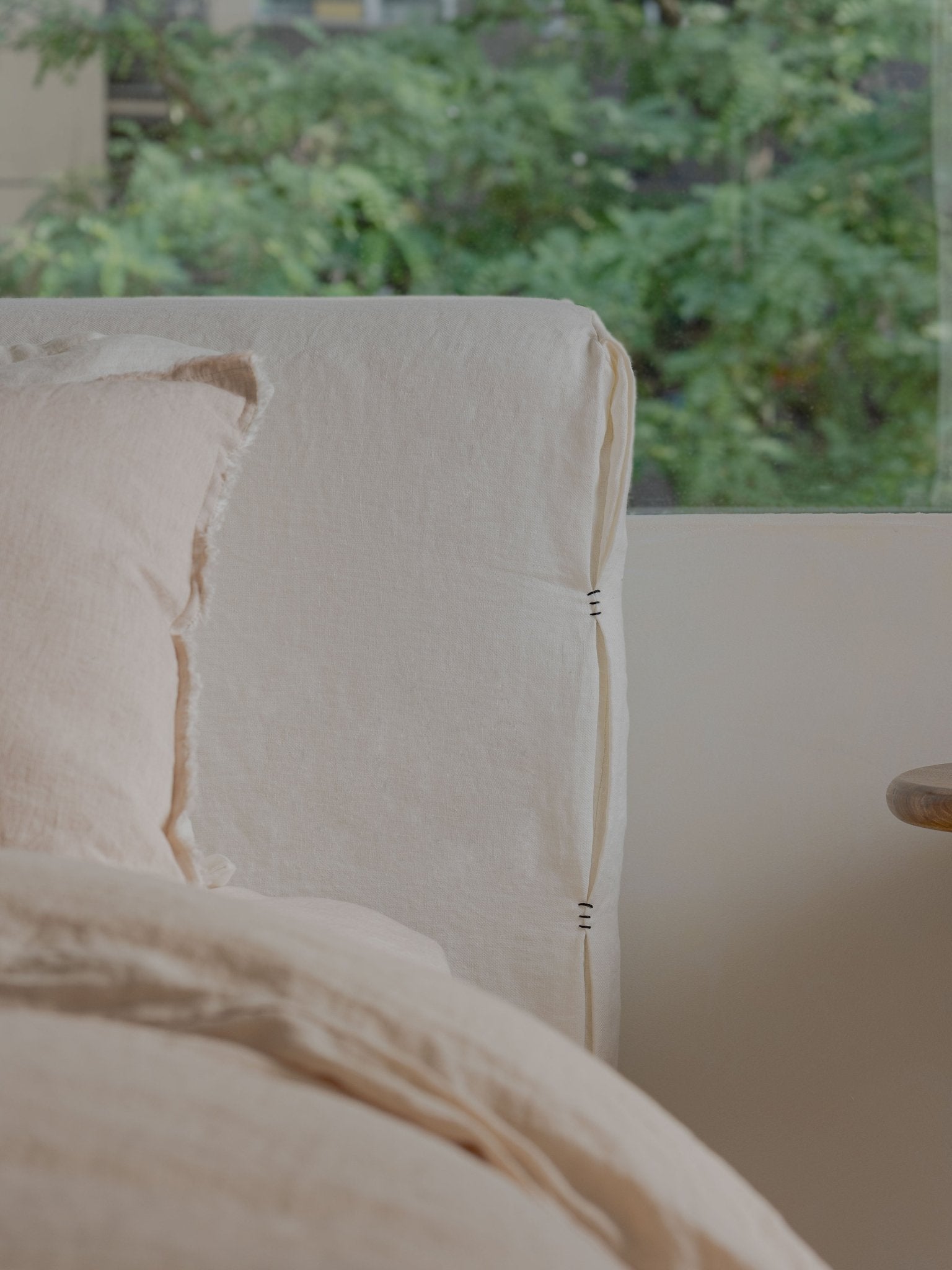 Freya Linen Bed detail: Cream linen headboard with visible stitching and a soft pillow, natural and peaceful design