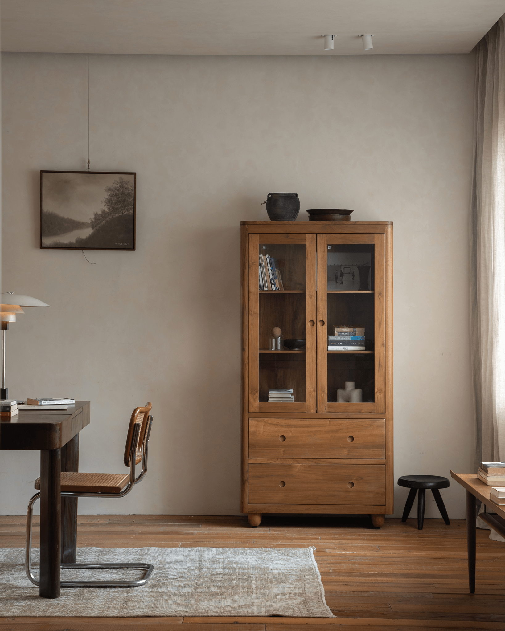 Reve Teak Bookcase in a cozy living room setting. Double glass doors and drawers in light teak wood.