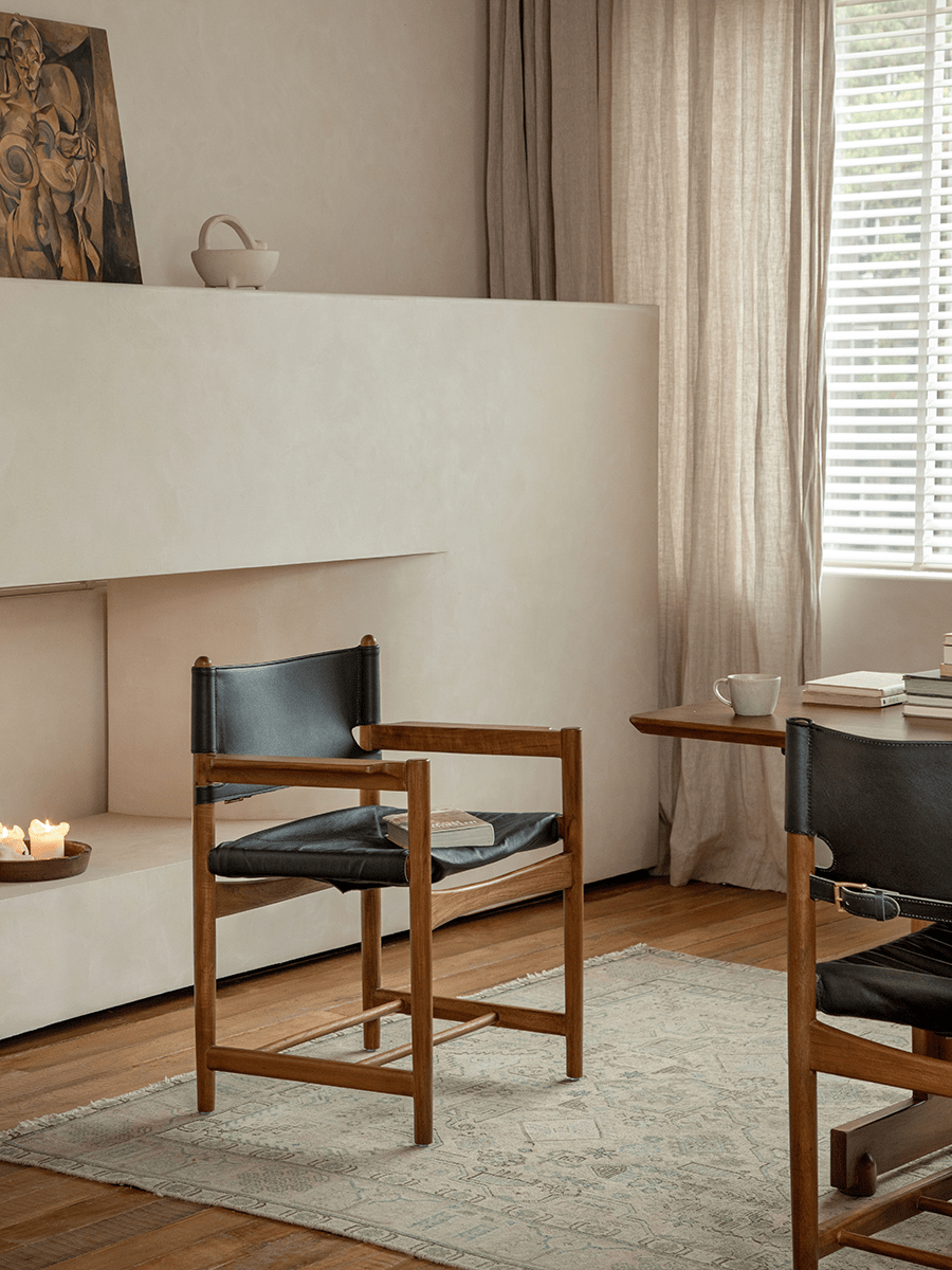 Spanish Dining Chair with black leather seat and teak wood frame in a neutral, cozy dining room setting