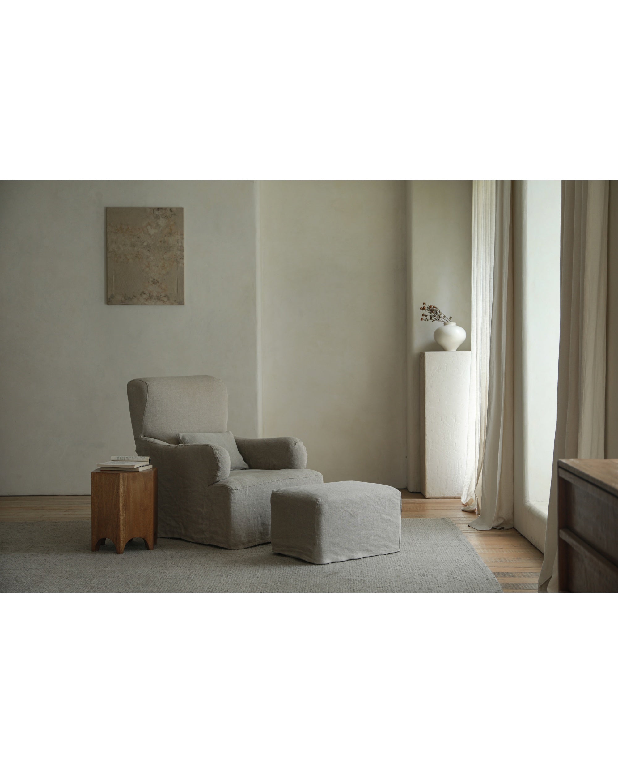 Neutral linen Eve Ottoman footrest paired with armchair and wooden side table.