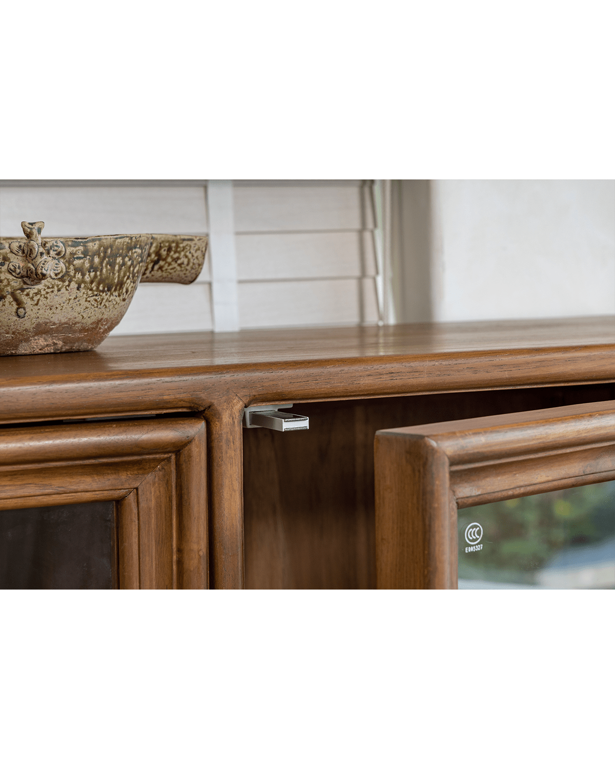 Teak wood Stilt Cabinet detail with glass door, metal handle, and ceramic bowl. Elegant dining room storage.
