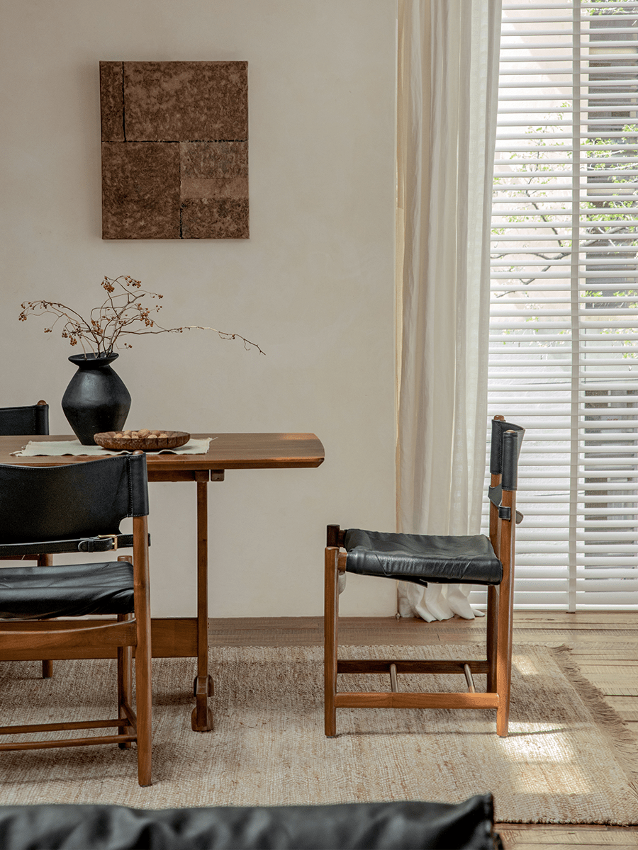 Spanish Dining Chair with black leather seat and teak wood frame in a bright, neutral dining room setting.
