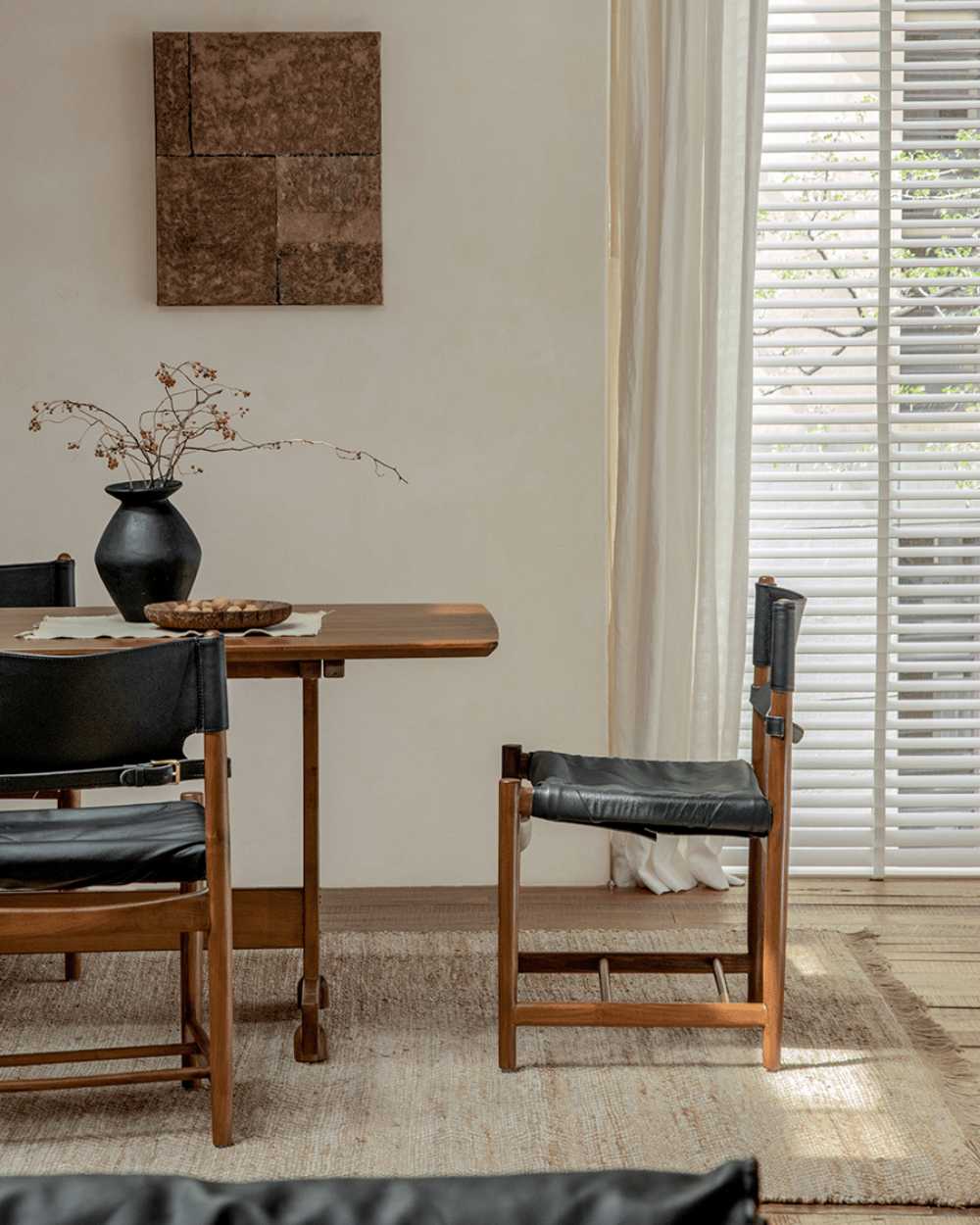 Spanish Dining Chair with black leather seat and teak wood frame in a bright, neutral dining room setting.