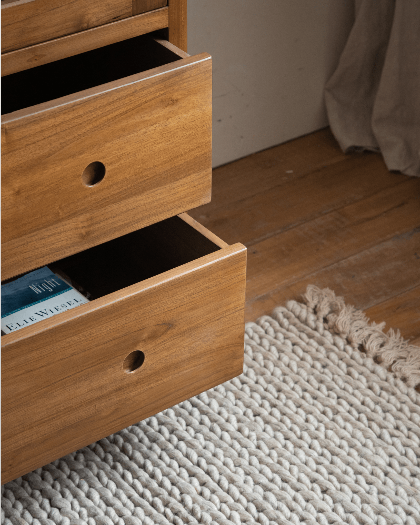 Reve Teak Bookcase drawer detail. Teak wood drawer with a book by Elie Wiesel, set on a textured rug.