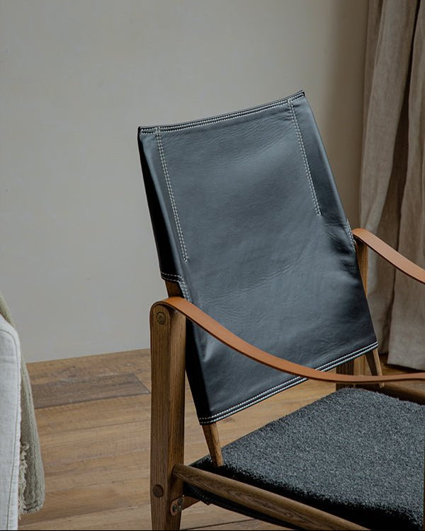 Safari Chair detail: Black leather backrest with white stitching, wooden frame, brown armrests, and gray seat.