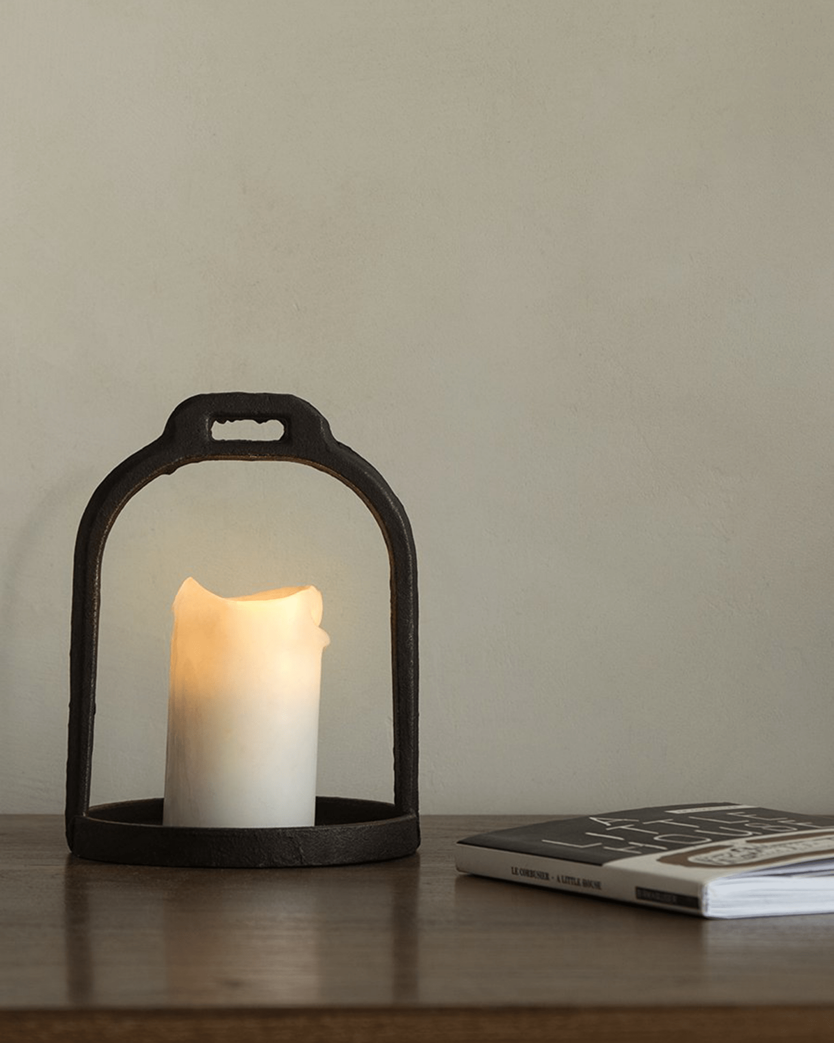 Rustic iron candle holder with lit candle, creating cozy ambiance. Accompanied by a book for home decor.