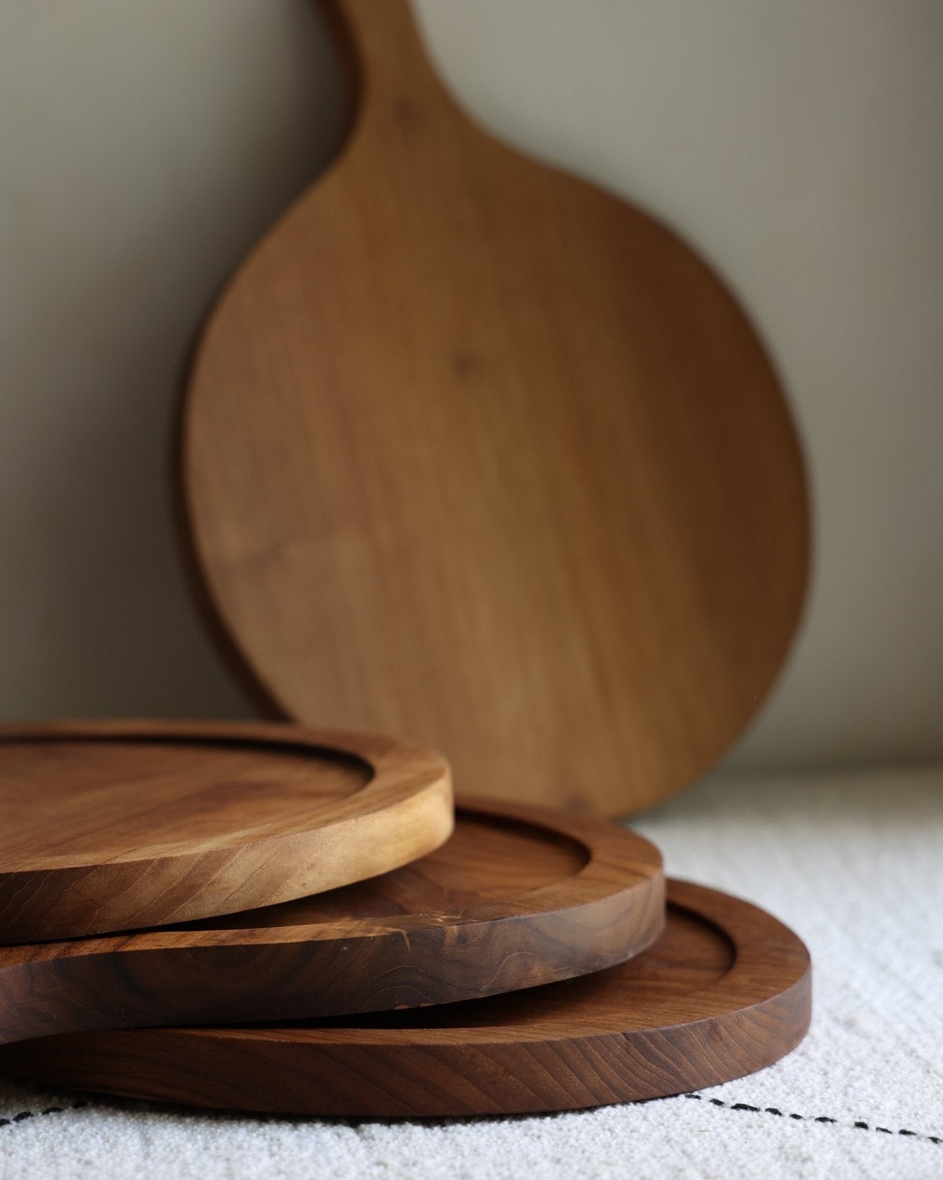 Round Teak Wood Butcher Block with serving boards stacked in front.