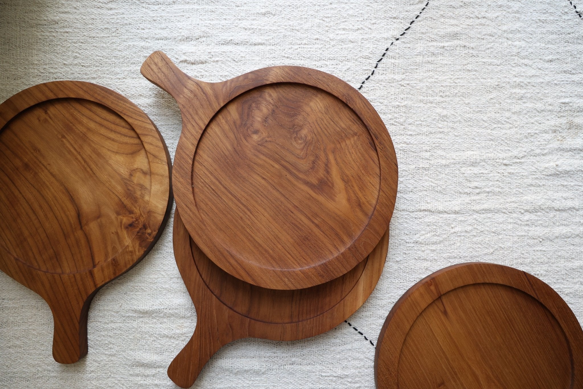 Ray Butcher Block: Round teak wood serving board with handle on textured cloth.