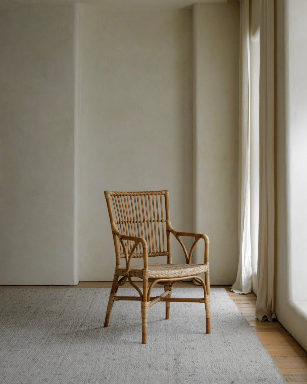 Axis Chair: natural Indonesian rattan armchair with woven seat and slatted back, on a grey rug.