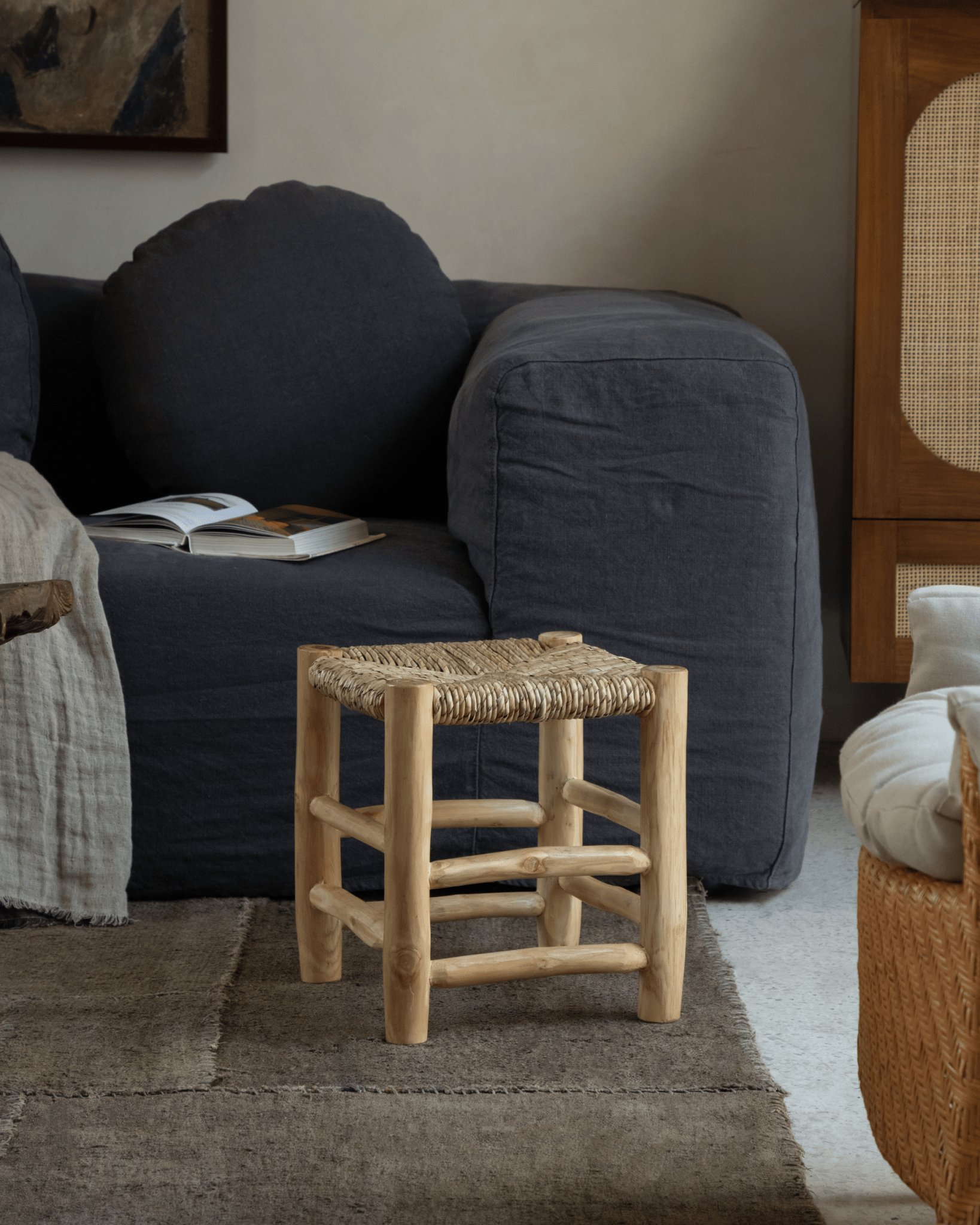 Isla Handwoven Stool in living room setting, natural teak frame and woven pandan seat.