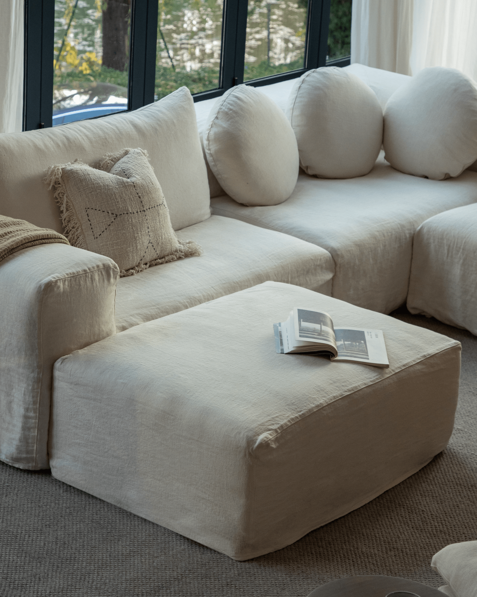 Doma Sectional Sofa in white linen, modular design, with book on ottoman. Relaxed, atmospheric living space.
