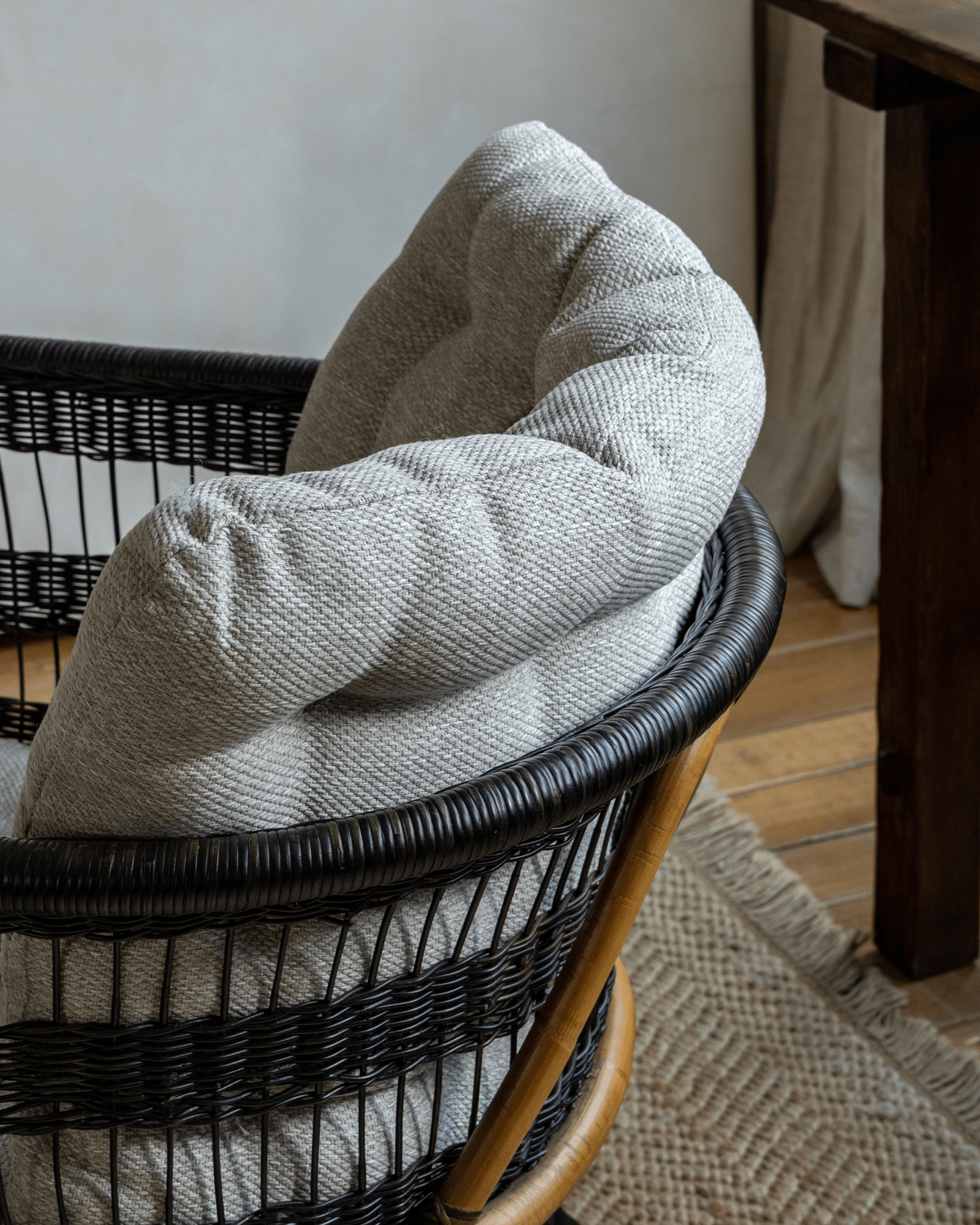 Helian Rattan Chair with gray silk cushion, black rattan frame and a cozy interior setting, stylish design