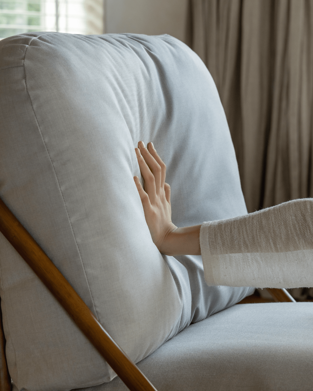 Hand touching light gray cushion of the Tofu Lounge Sofa, promoting relaxation.