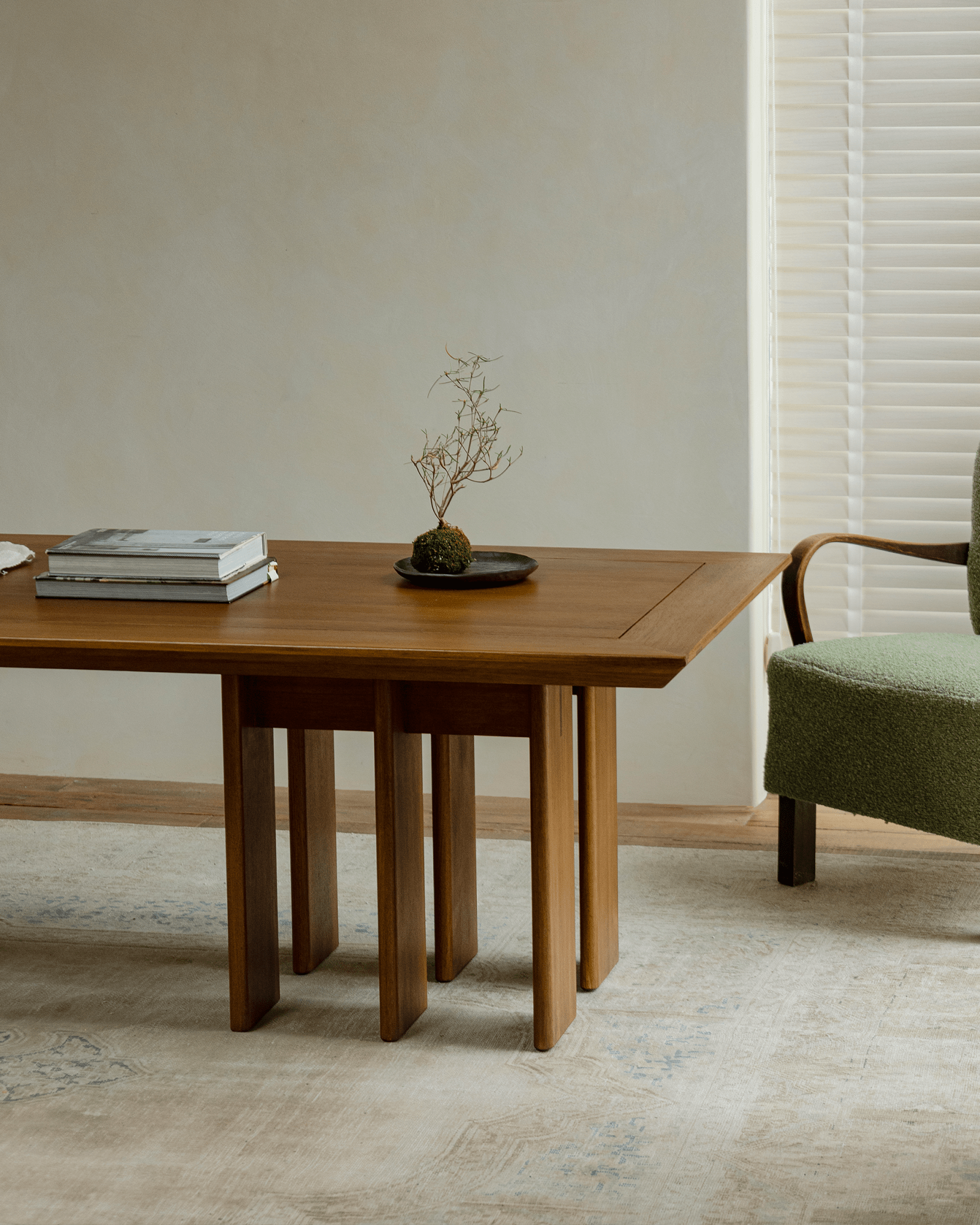 Titan Teak Dining Table in a modern setting with teak wood, multi-leg design, and stylish green armchair