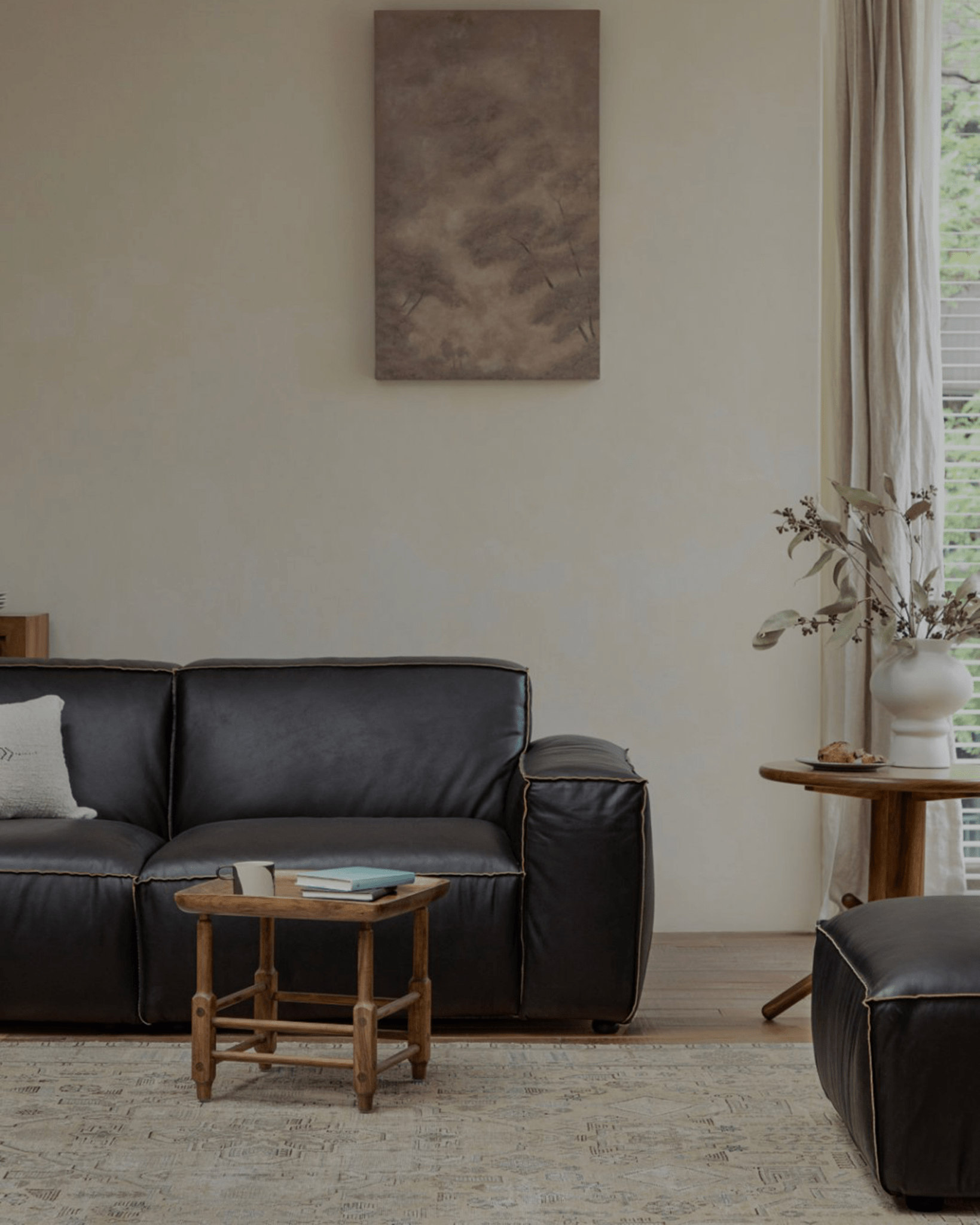 Modern living room with dark leather sofa, wooden furniture, and rug.