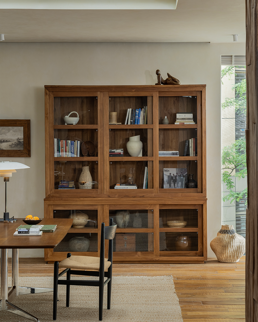 Teak wood glass front bookcase with sliding glass doors, displaying books and decor in a stylish living room setting.